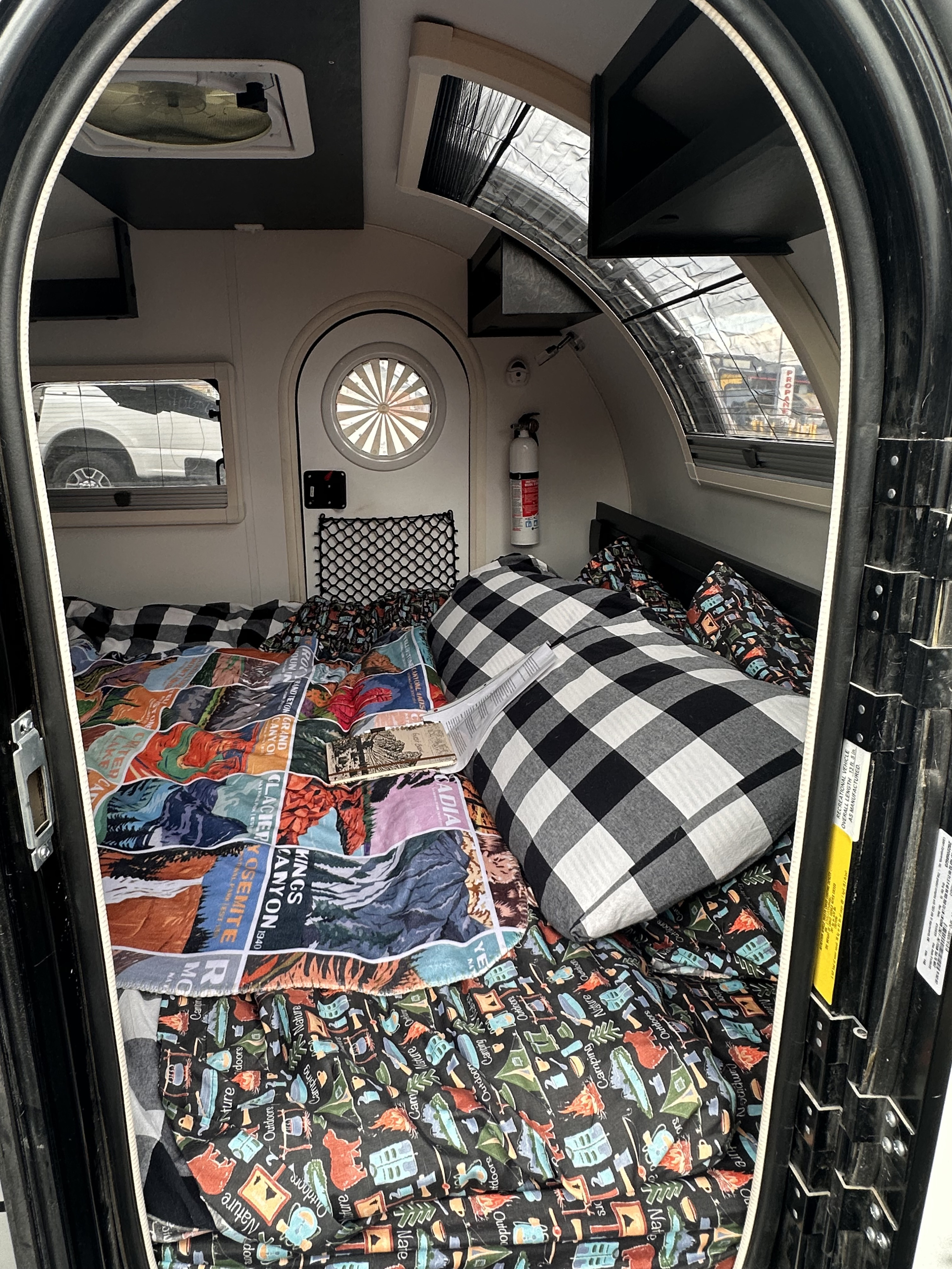 Inside a compact RV rental, featuring a cozy bed with patterned blankets, windows, and an overhead fan.. nuCamp T@G 2023