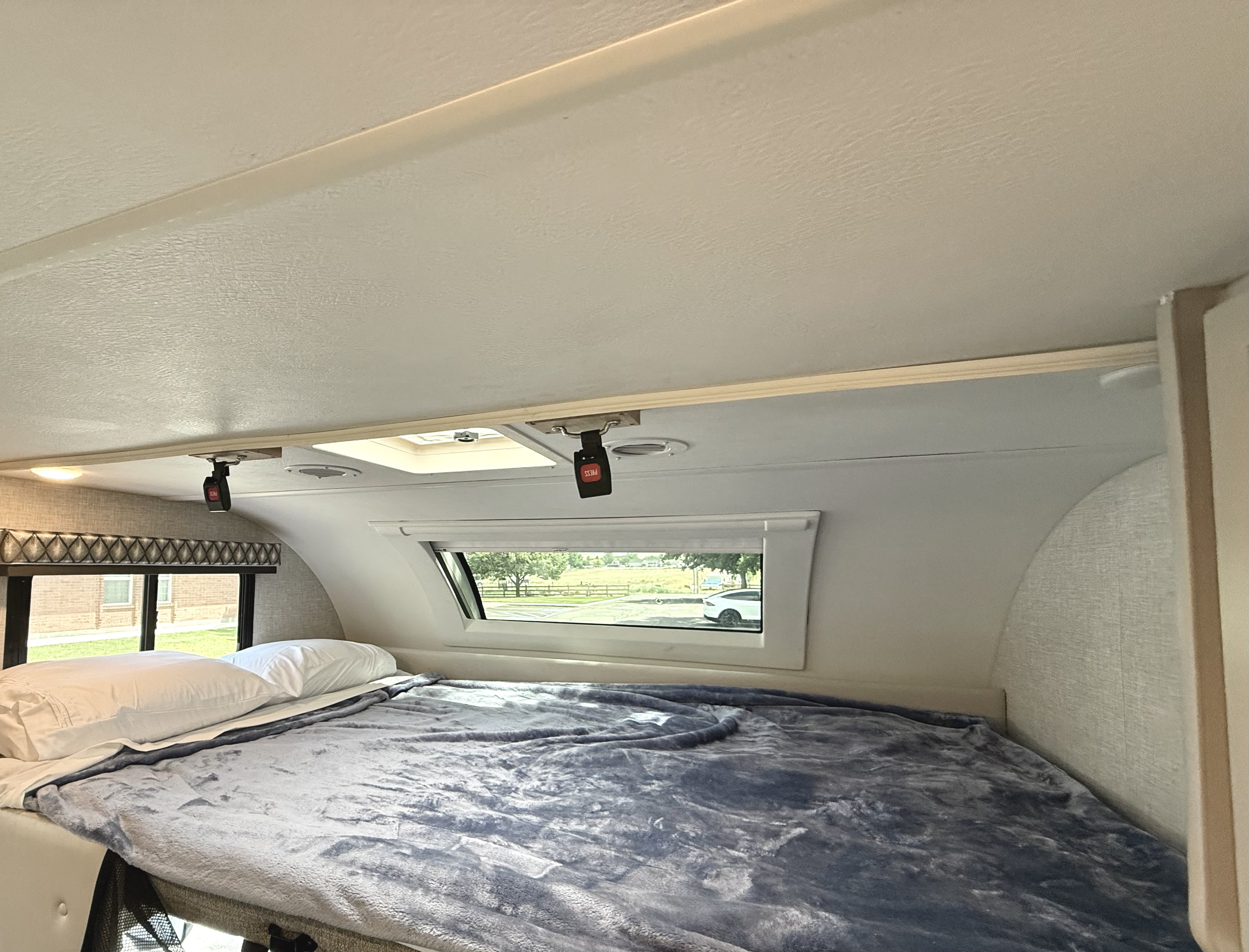 Inside a comfortable RV rental: a plush bed, wide windows with outdoor views, and a ceiling skylight.. Thor Geneva 2022