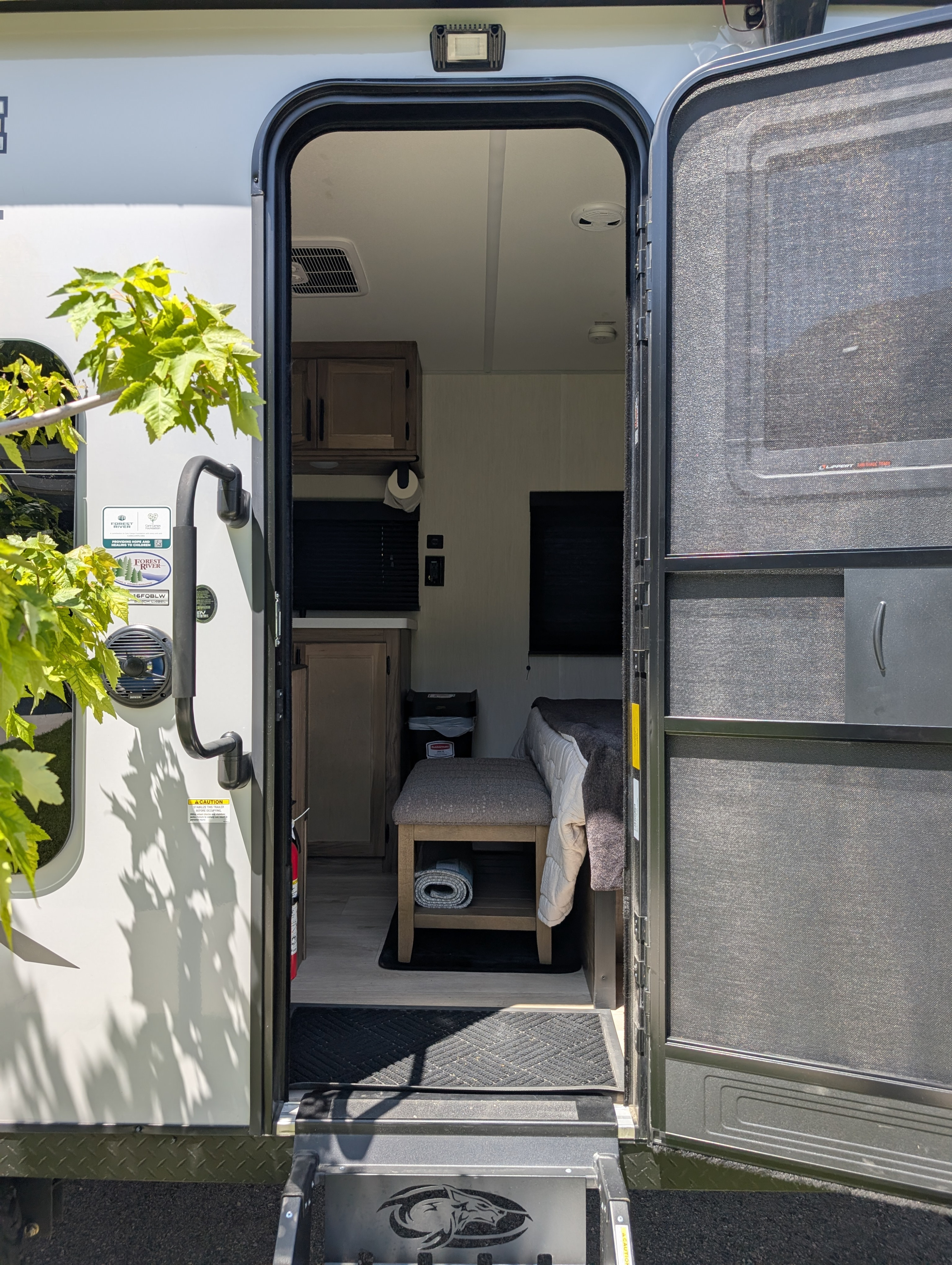 RV rental interior view: steps lead into a cozy camper with bed & kitchenette, screen door open.. Forest River 16FQBLW 2025