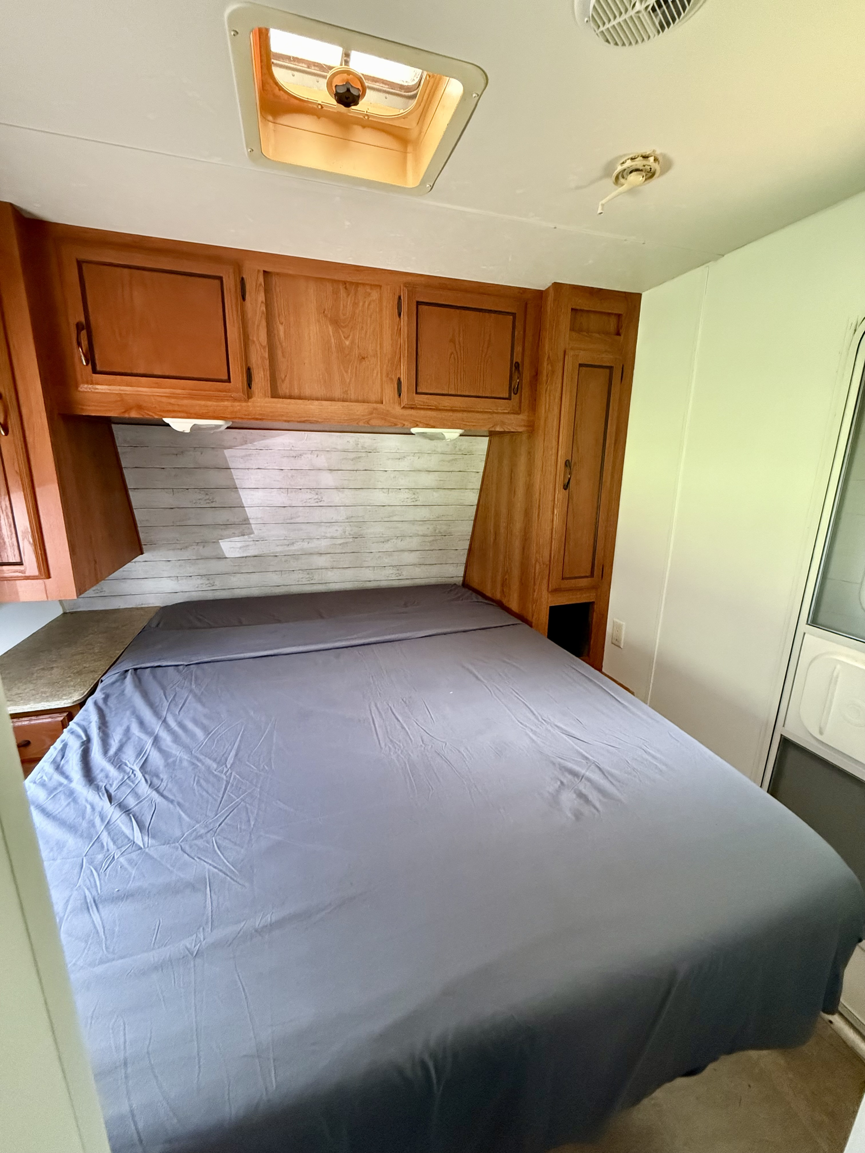 RV rental bedroom with gray bed, wooden cabinets, shiplap accent wall, and ceiling skylight.. Forest River Coachmen Catalina 2010