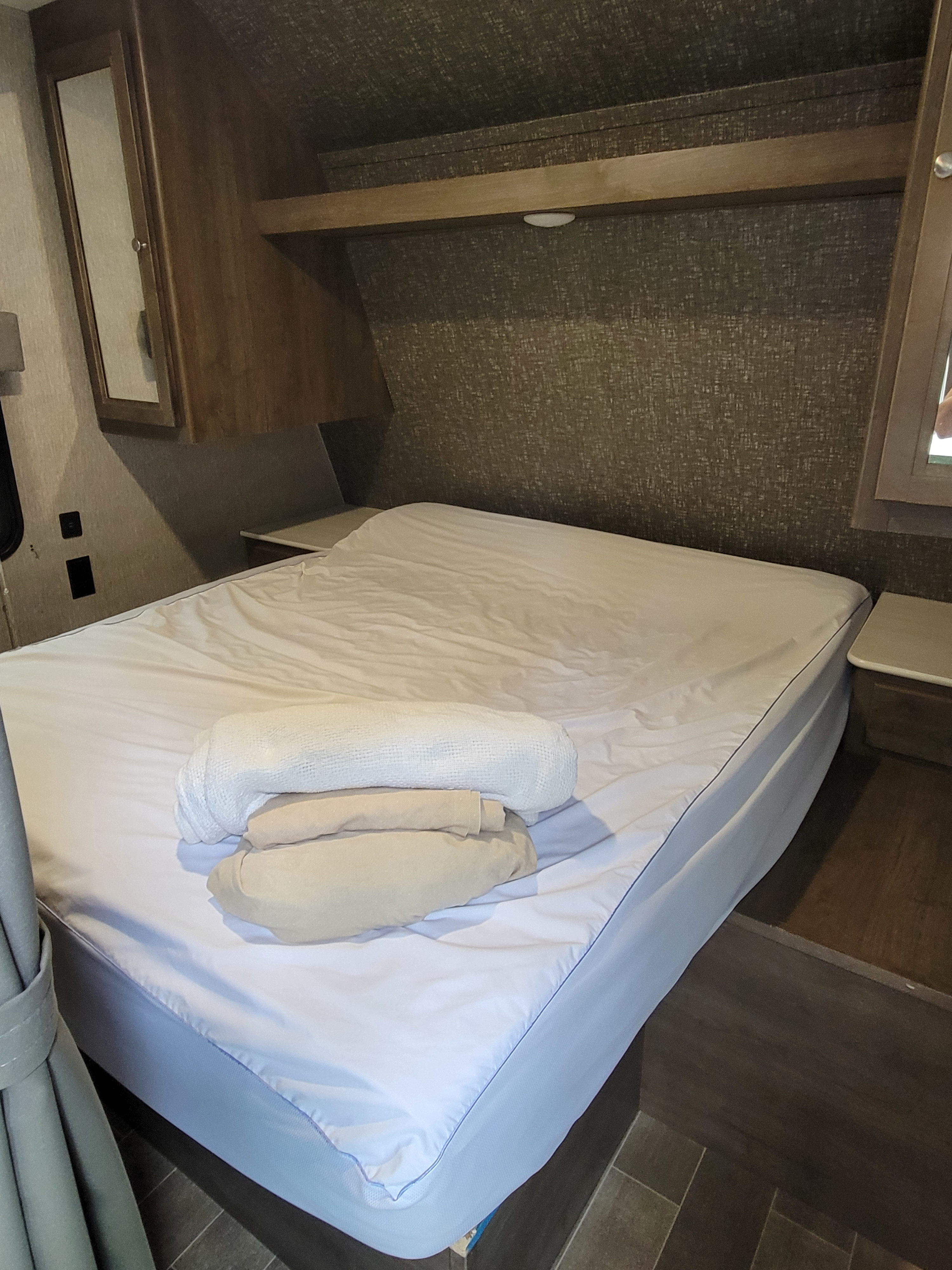Comfortable RV rental bedroom with a neatly made bed, white sheets, folded towels, and overhead storage.. Keystone Coleman Lantern 2019