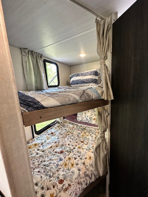 An RV rental features two comfortable bunk beds with colorful bedding and windows.. No Boundaries 19.3 2020