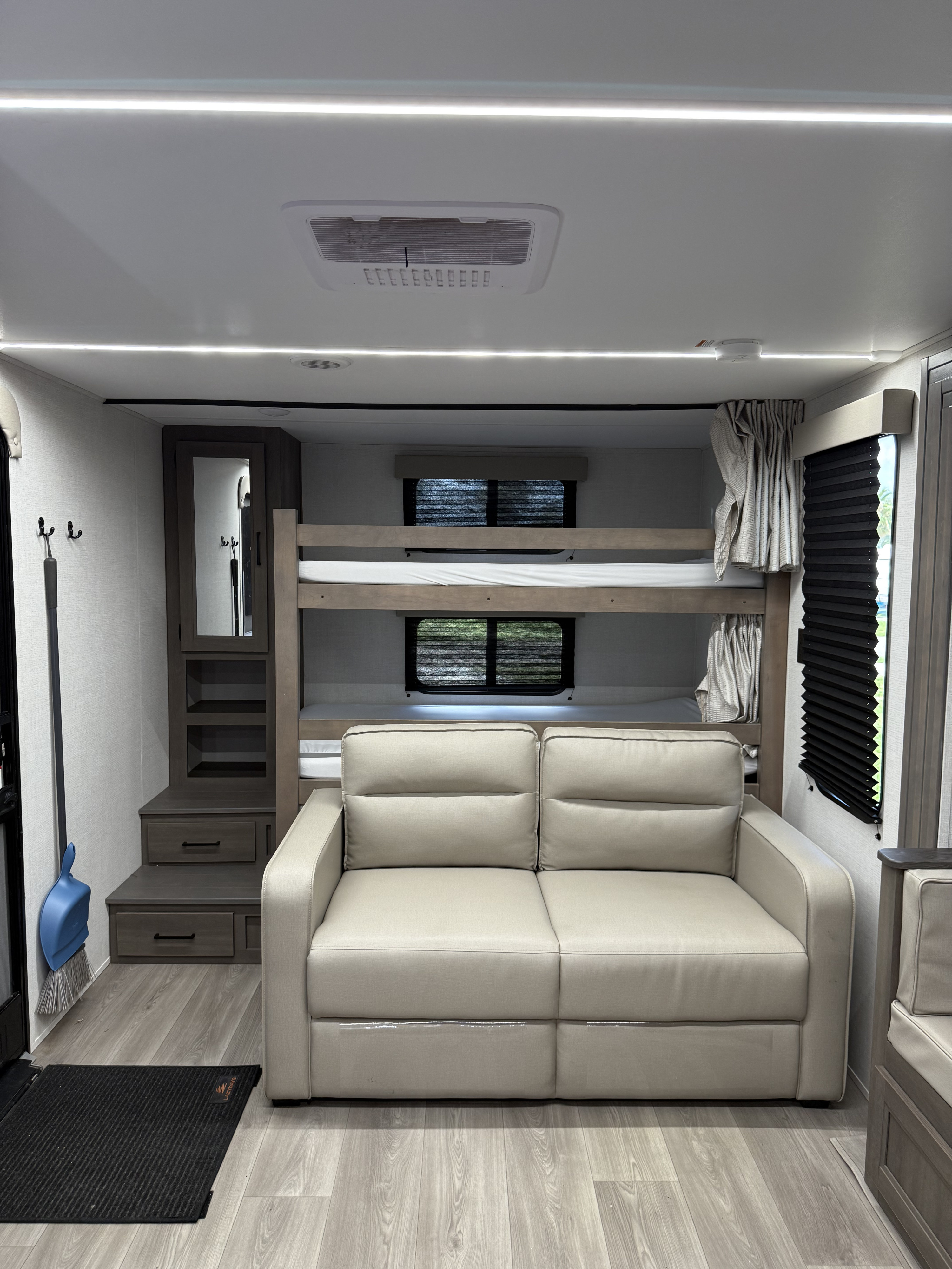 Modern **rv rental** interior featuring a light-colored sofa, bunk beds, and built-in storage, ideal for family travel.. Grand Design 265-BHT 2025