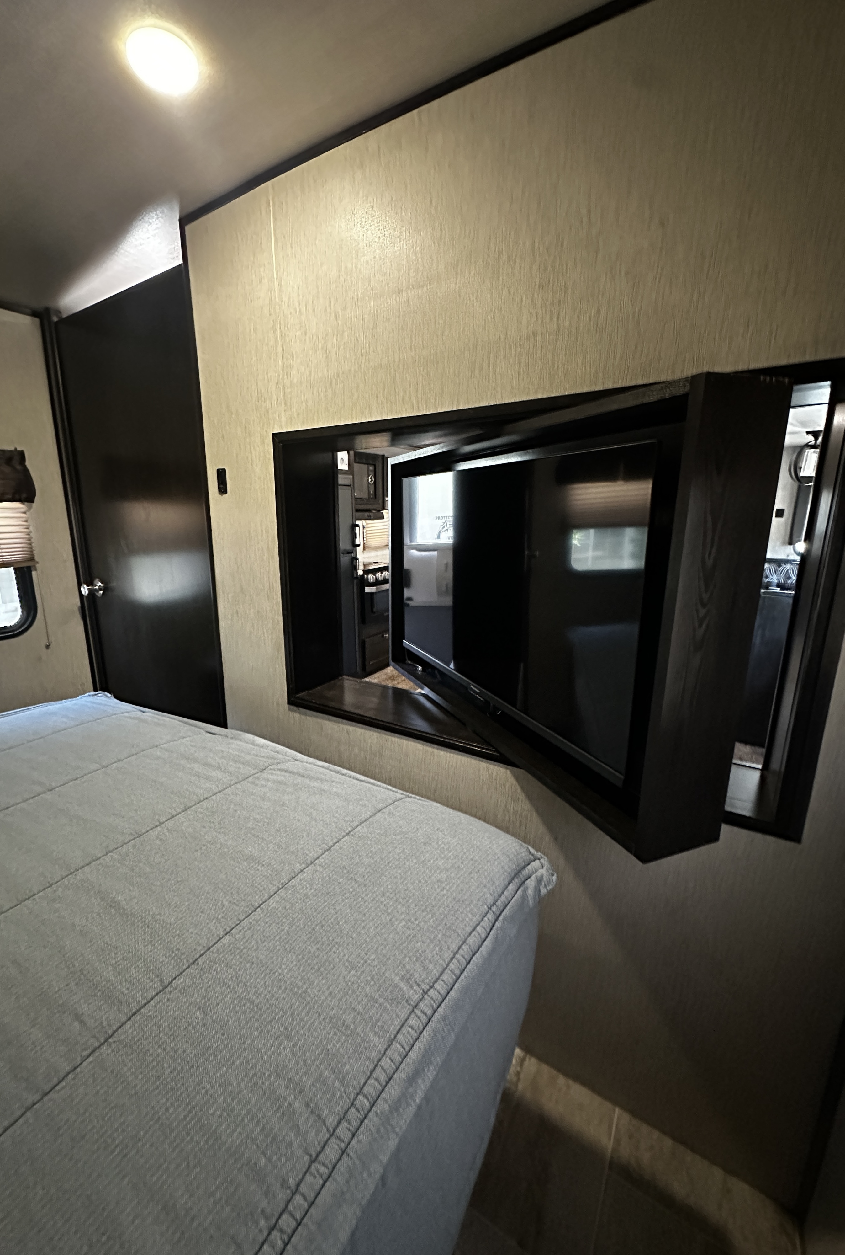 RV rental bedroom featuring a bed, a swing-out TV, and a view into the compact living area with a kitchen.. Heartland RVs North Trail 2018