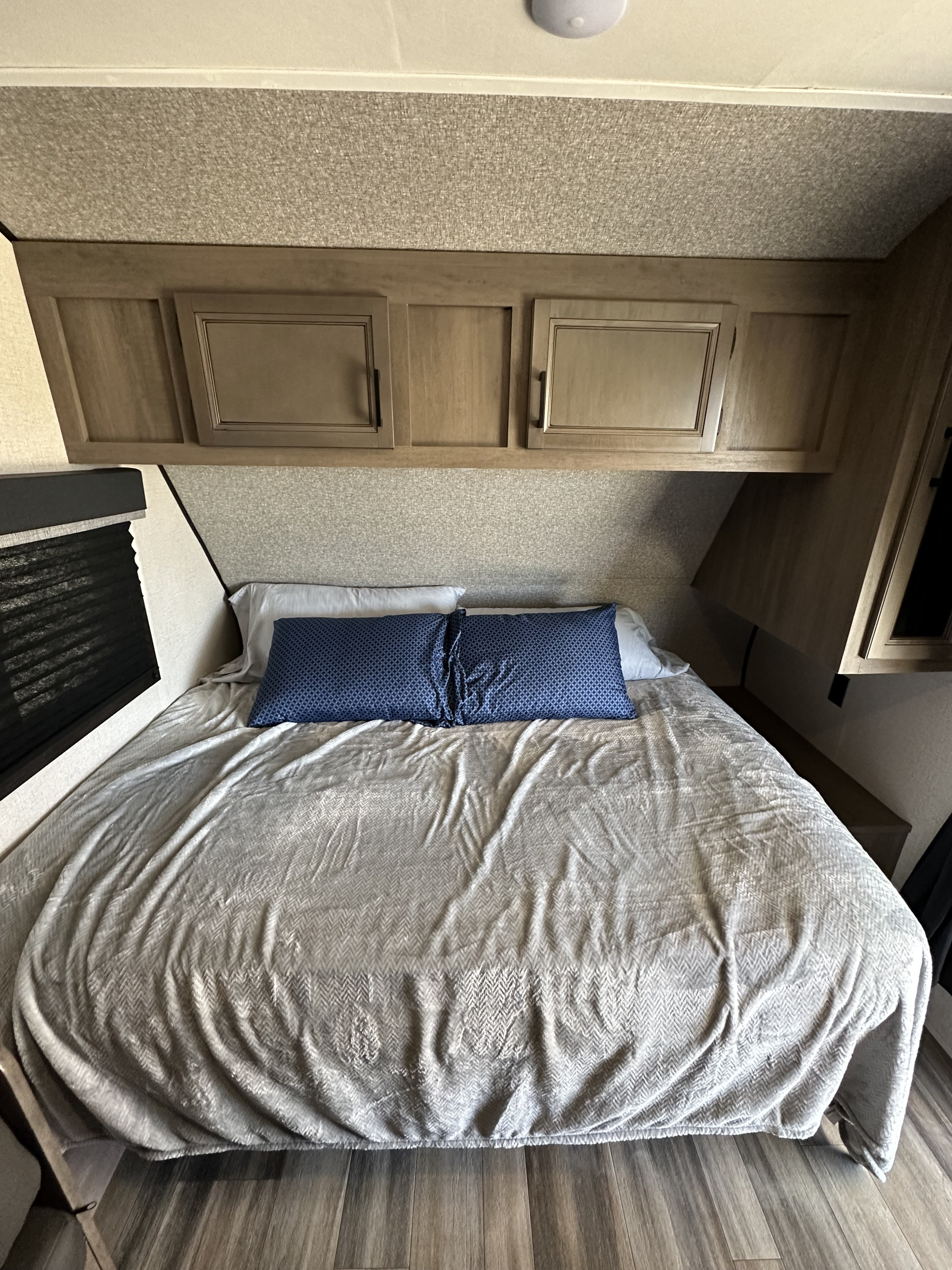 Inside an RV rental: a compact bedroom featuring a bed, blue pillows, wooden storage cabinets, and a window.. Starcraft Autumn Ridge 2022