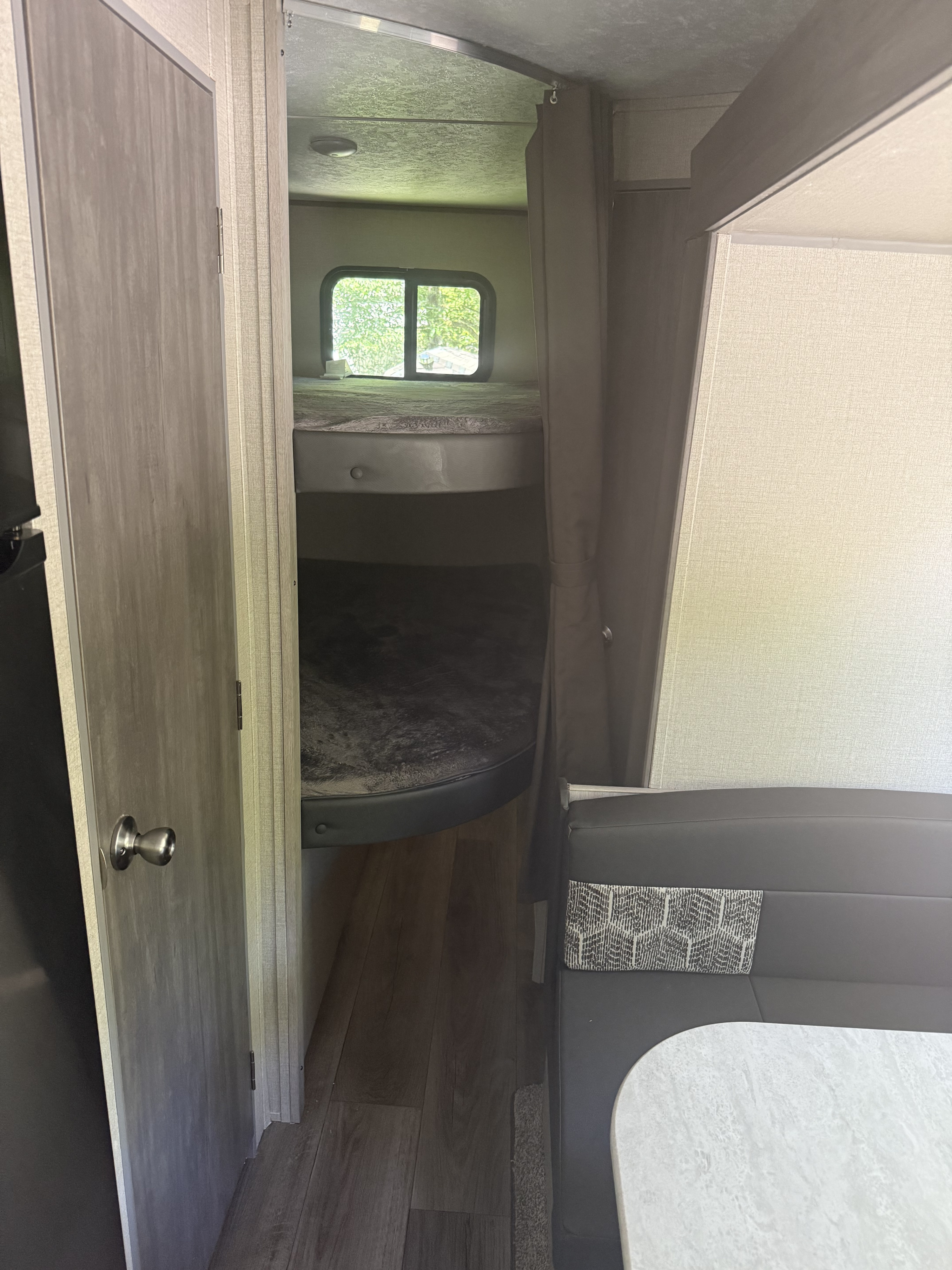 An RV rental interior with bunk beds, a large window, and a dinette featuring a gray bench and light table.. Coachmen 2022 Coachmen Catalina 28BHS 2022