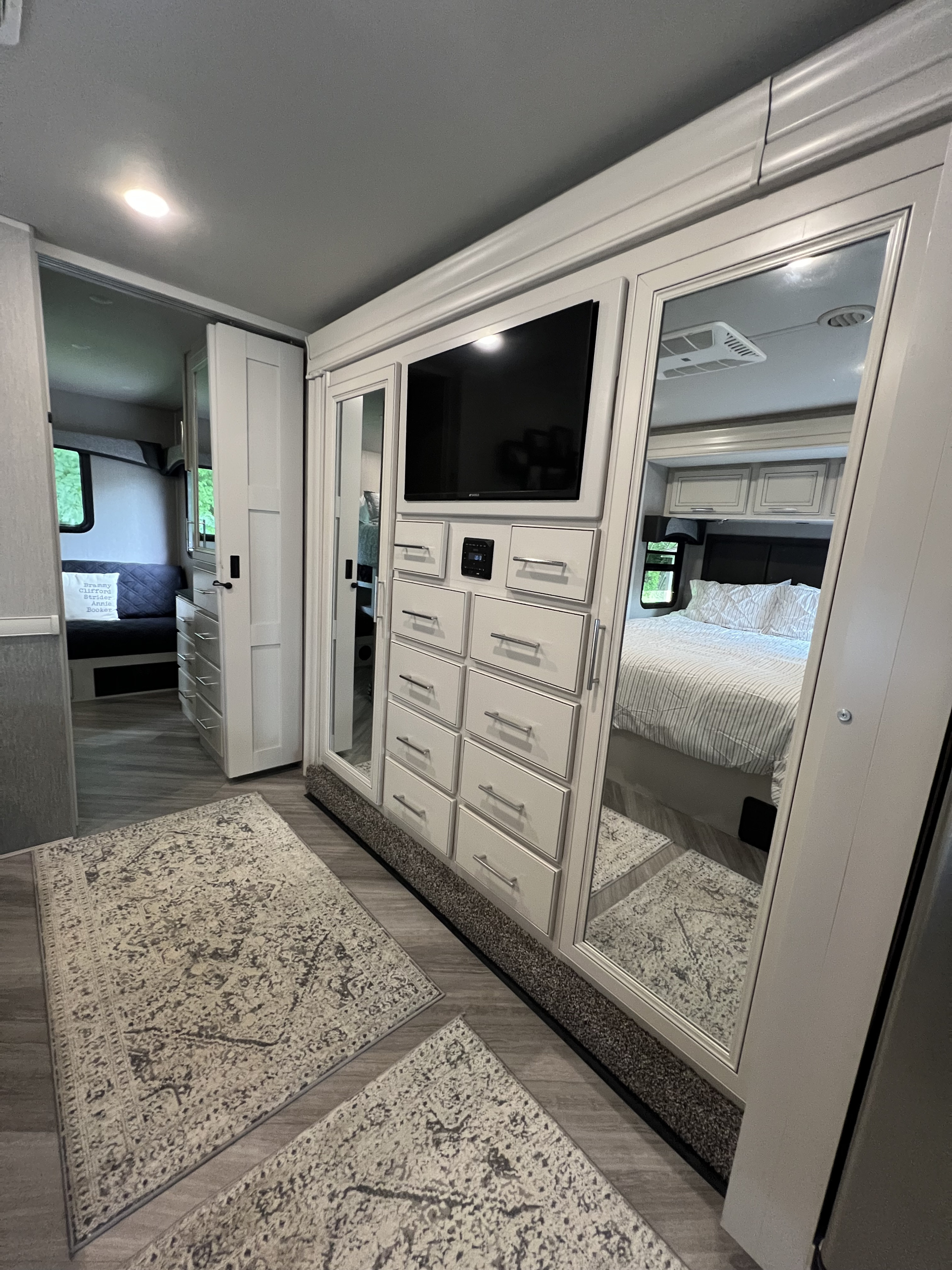 Spacious RV rental interior showcases a modern bedroom (reflection), central TV/storage unit, and light wood-look flooring.. Fleetwood Fortis 2024