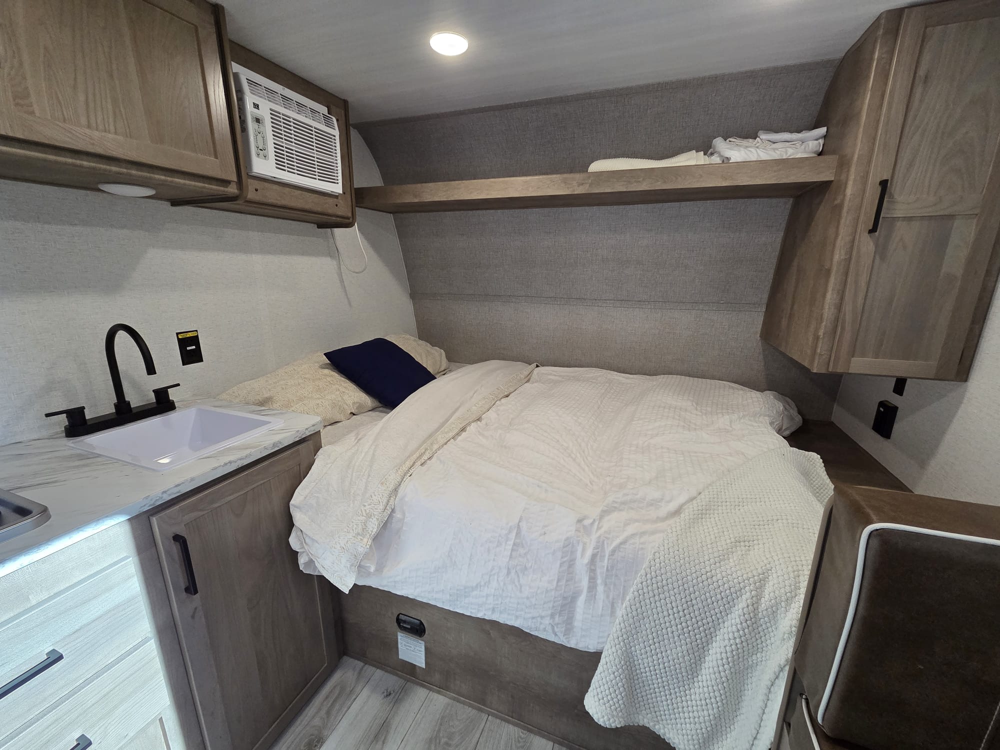 RV rental interior featuring a cozy bed, small kitchen with sink, AC unit, and storage cabinets for compact living.. Keystone Springdale 1400RE 2025