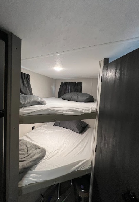RV rental interior features cozy bunk beds with grey bedding, providing a compact and comfortable sleeping area.. Forest River ozark 2021