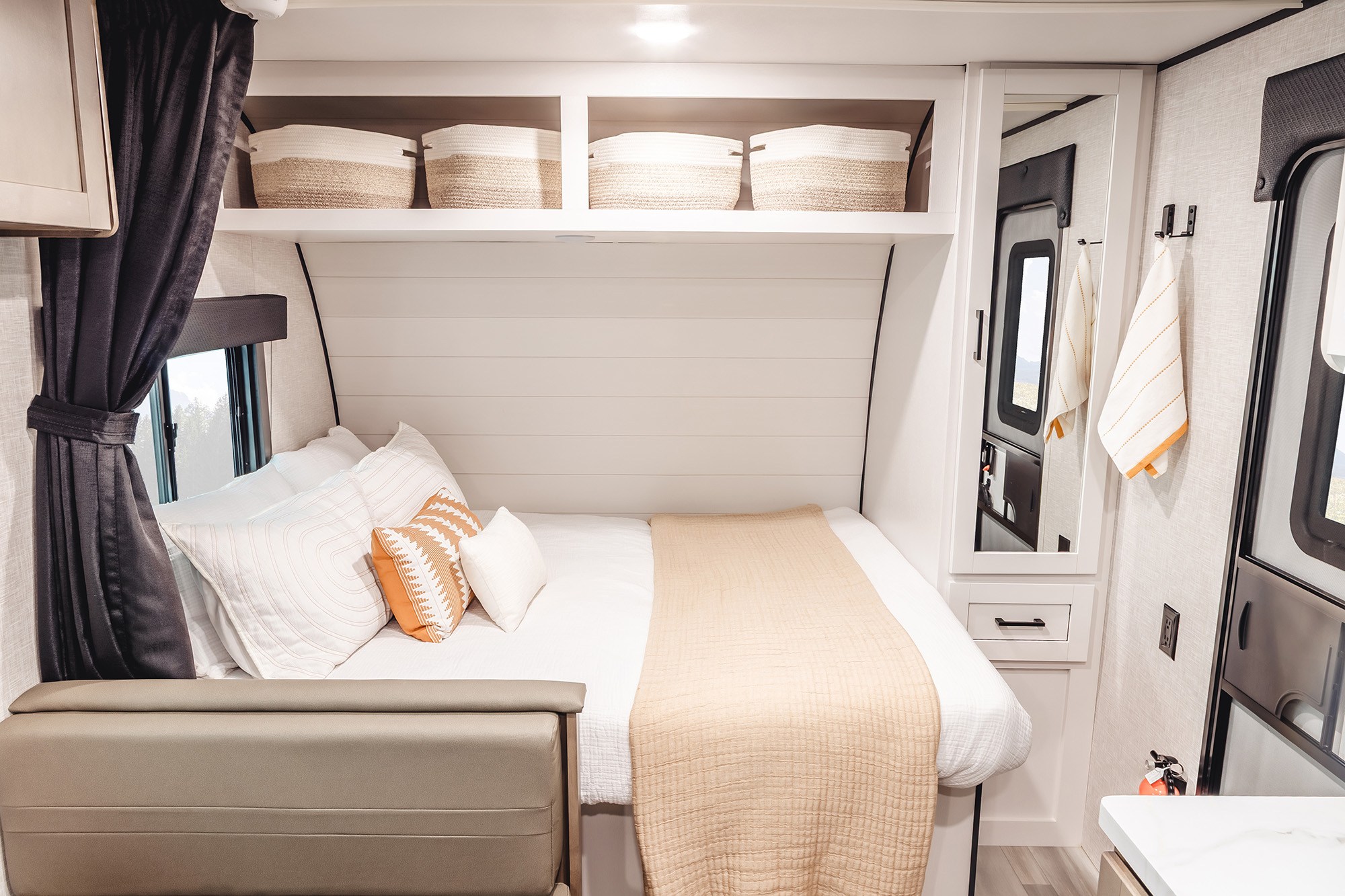 Cozy RV rental bedroom featuring a neatly made bed, decorative pillows, overhead storage with baskets, and a window with dark curtains.. Wayfinder RV Go Play 19BH 2025
