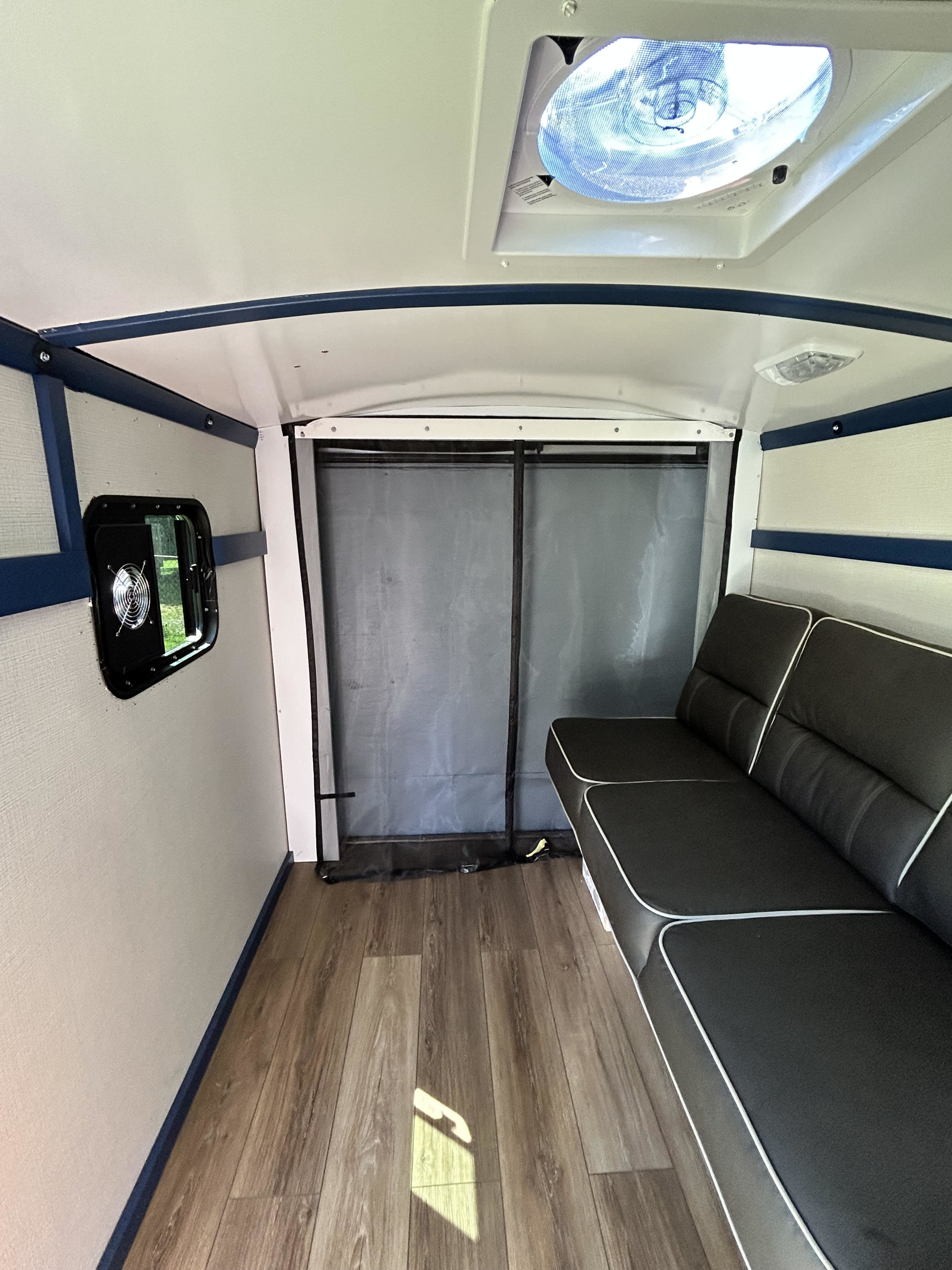 RV rental interior: black sofa, wood floor, blue trim, window fan, and ceiling vent. A bright and functional space.. Custom Camper 1999