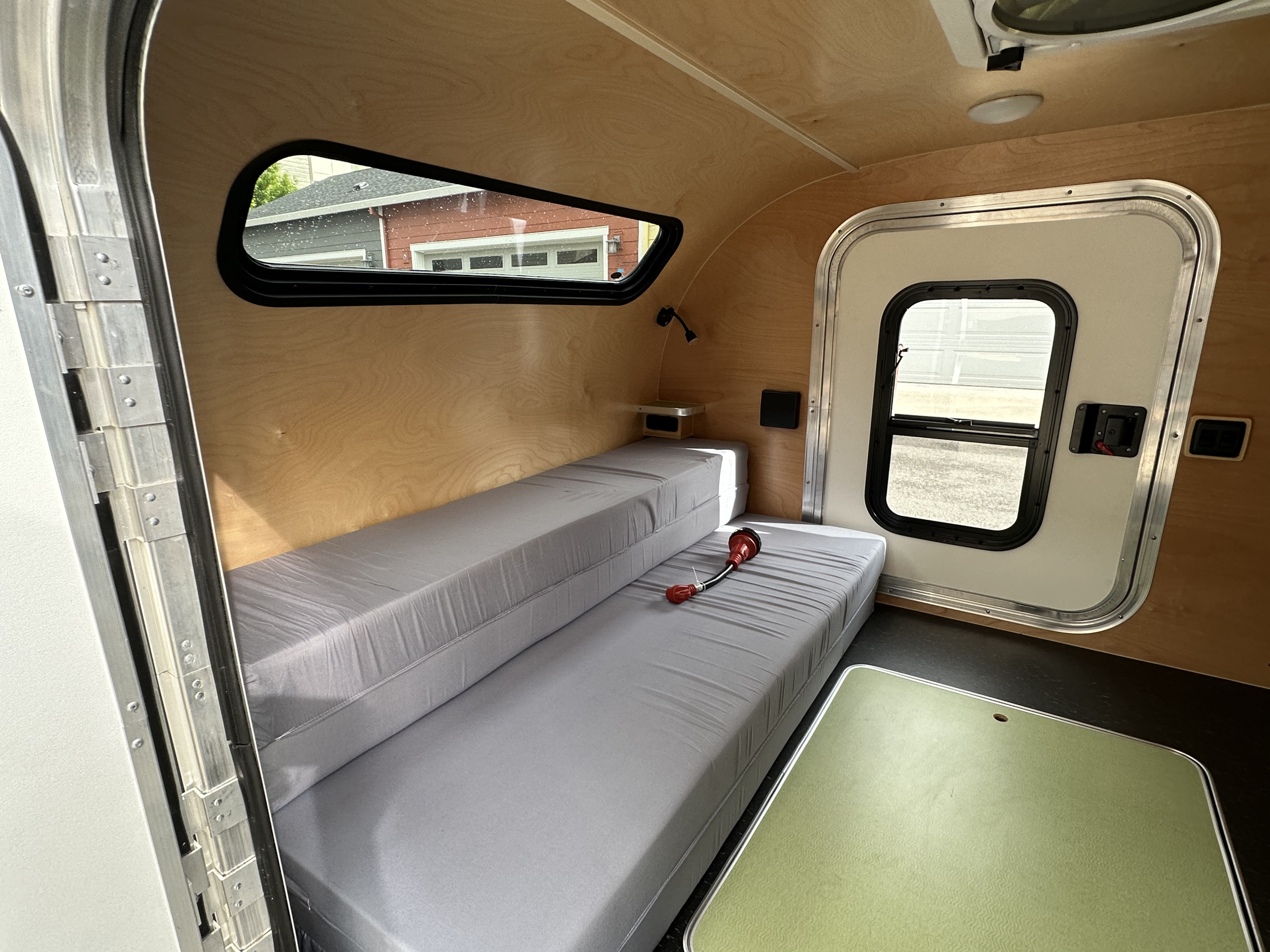 Inside a compact RV rental: light wood paneling, grey convertible beds/seating, and windows offering natural light. Ideal for travel.. Aero Teardrops Steel HC 2021