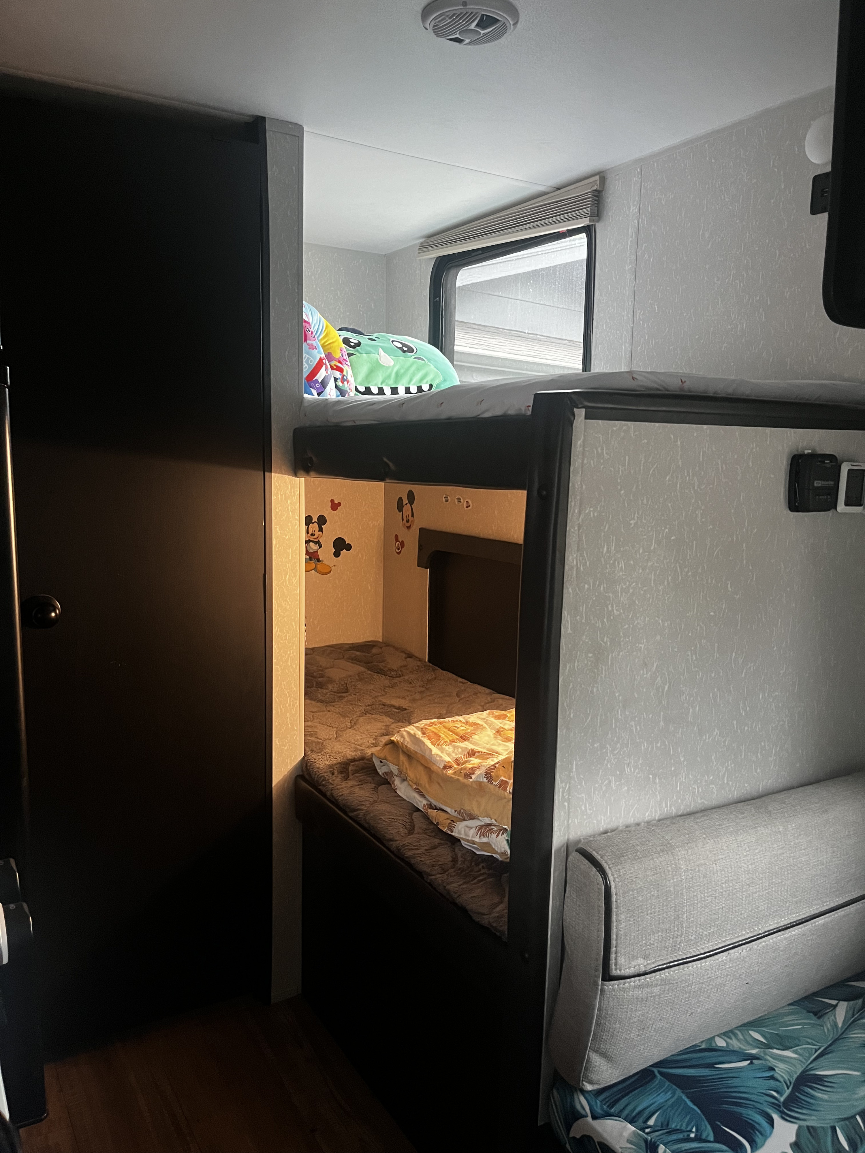 An RV rental's cozy bunk bed sleeping area with window, Mickey Mouse decals, and comfy bedding for adventures.. Forest River Cherokee Wolf Pup Black Label 2021