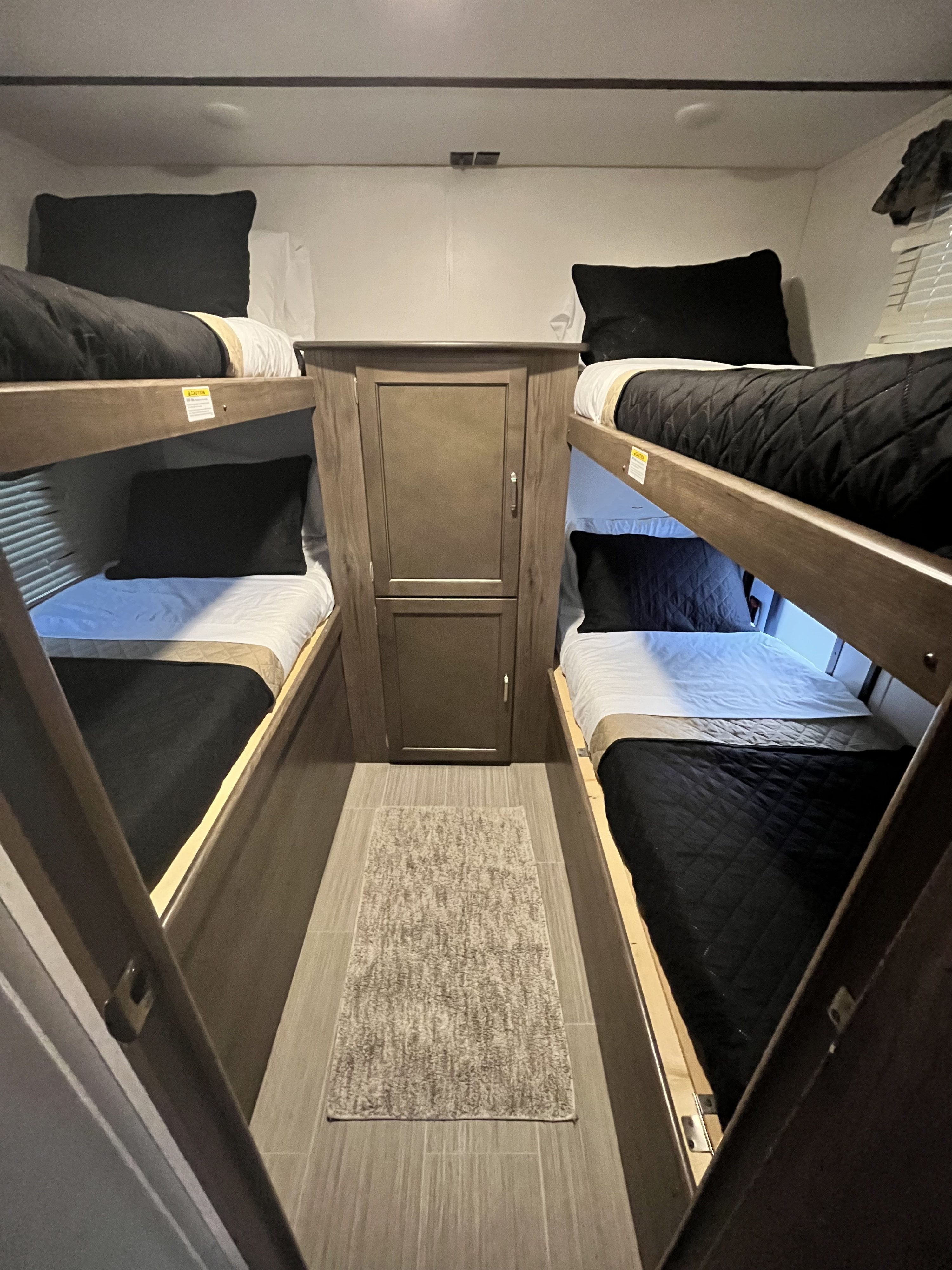 Four comfy bunk beds inside an RV rental. Dark bedding, central cabinet, and rug create a welcoming sleep space.. Keystone RV Passport Grand Touring 2019