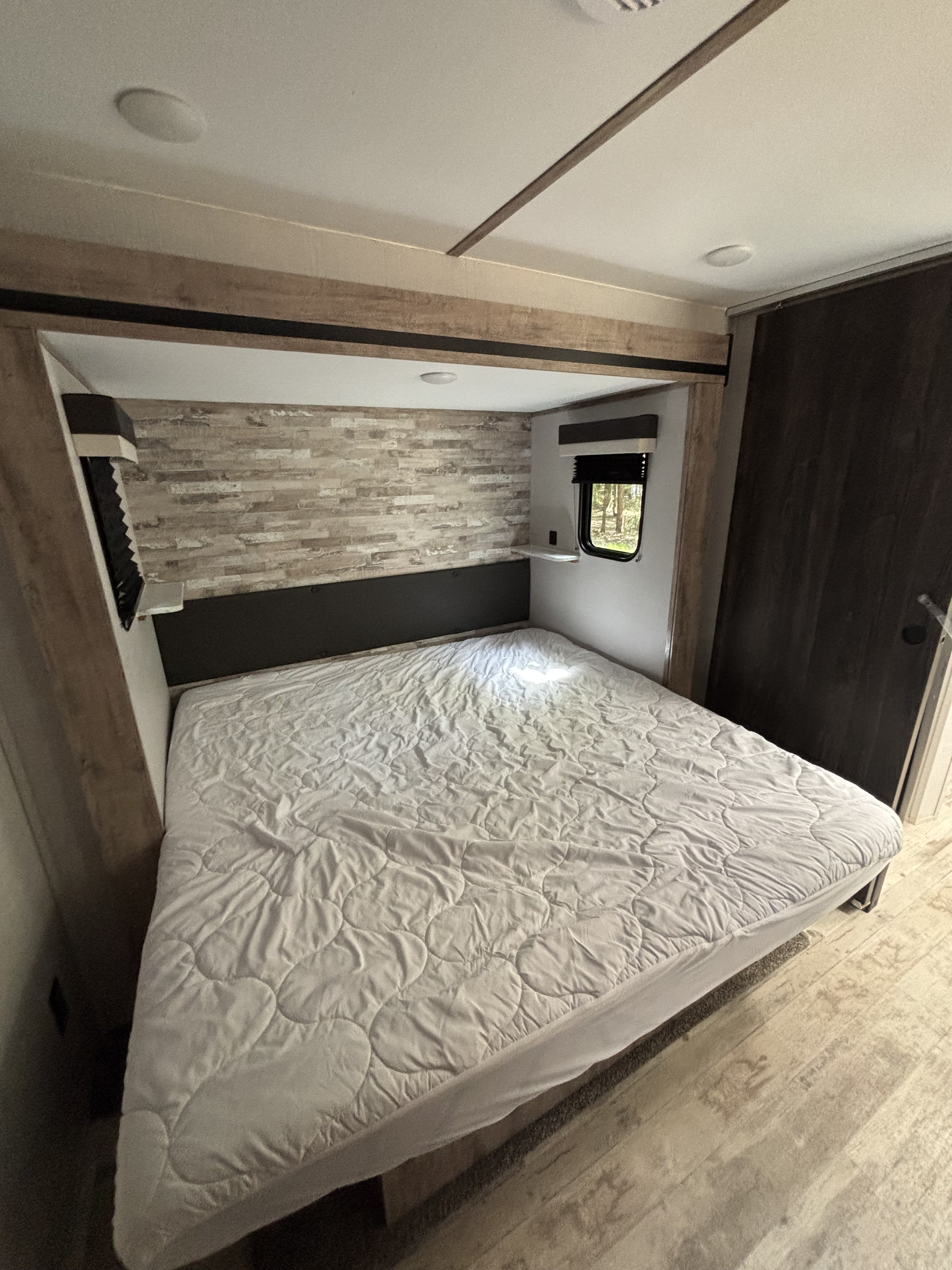 This compact RV rental bedroom features a comfy bed, textured headboard, and a window overlooking nature.. Gulf Stream Innsbruck 2023