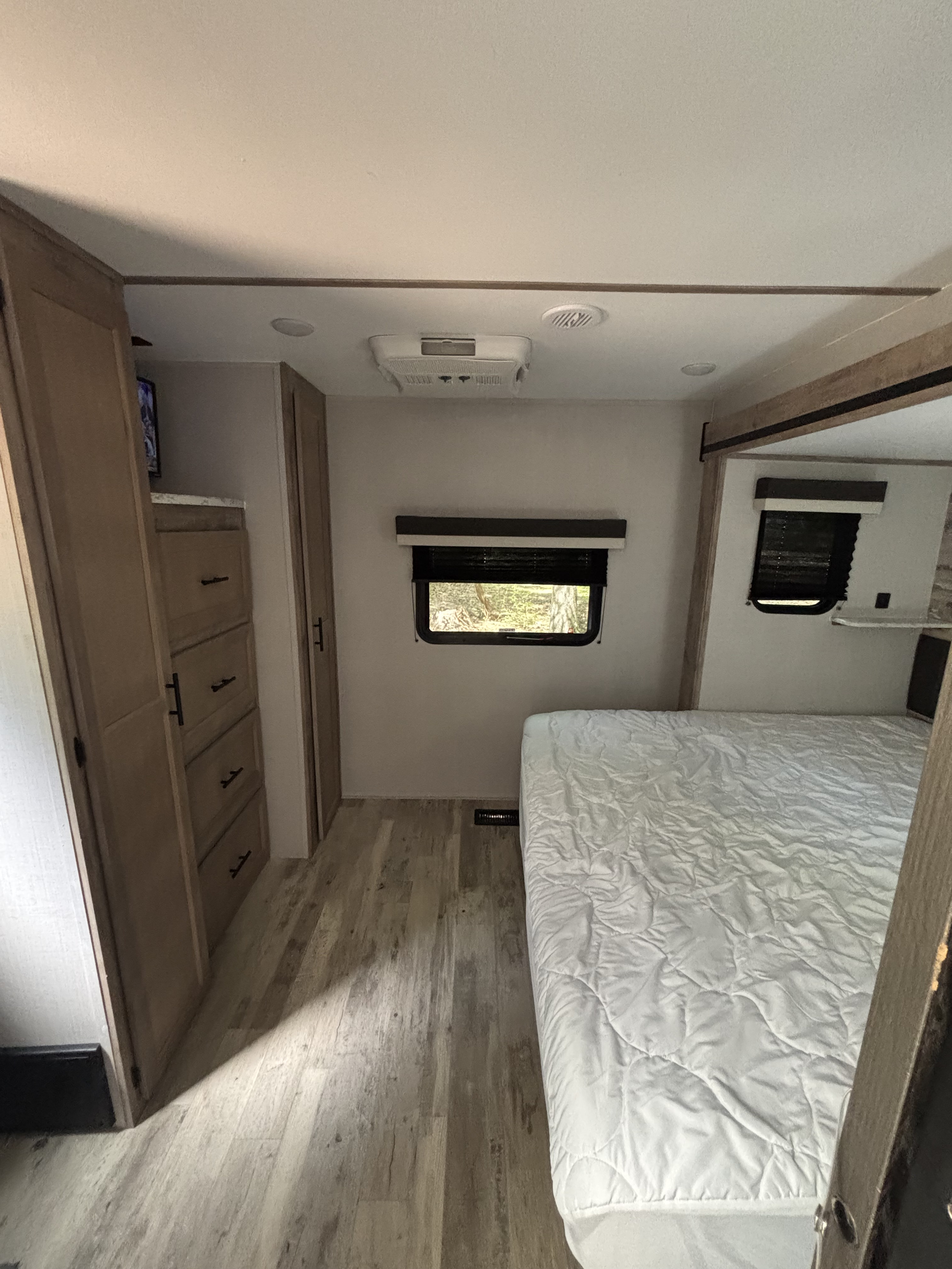 Clean RV rental bedroom showing a bed, built-in dresser, windows, and ceiling AC unit. Ready for travel.. Gulf Stream Innsbruck 2023