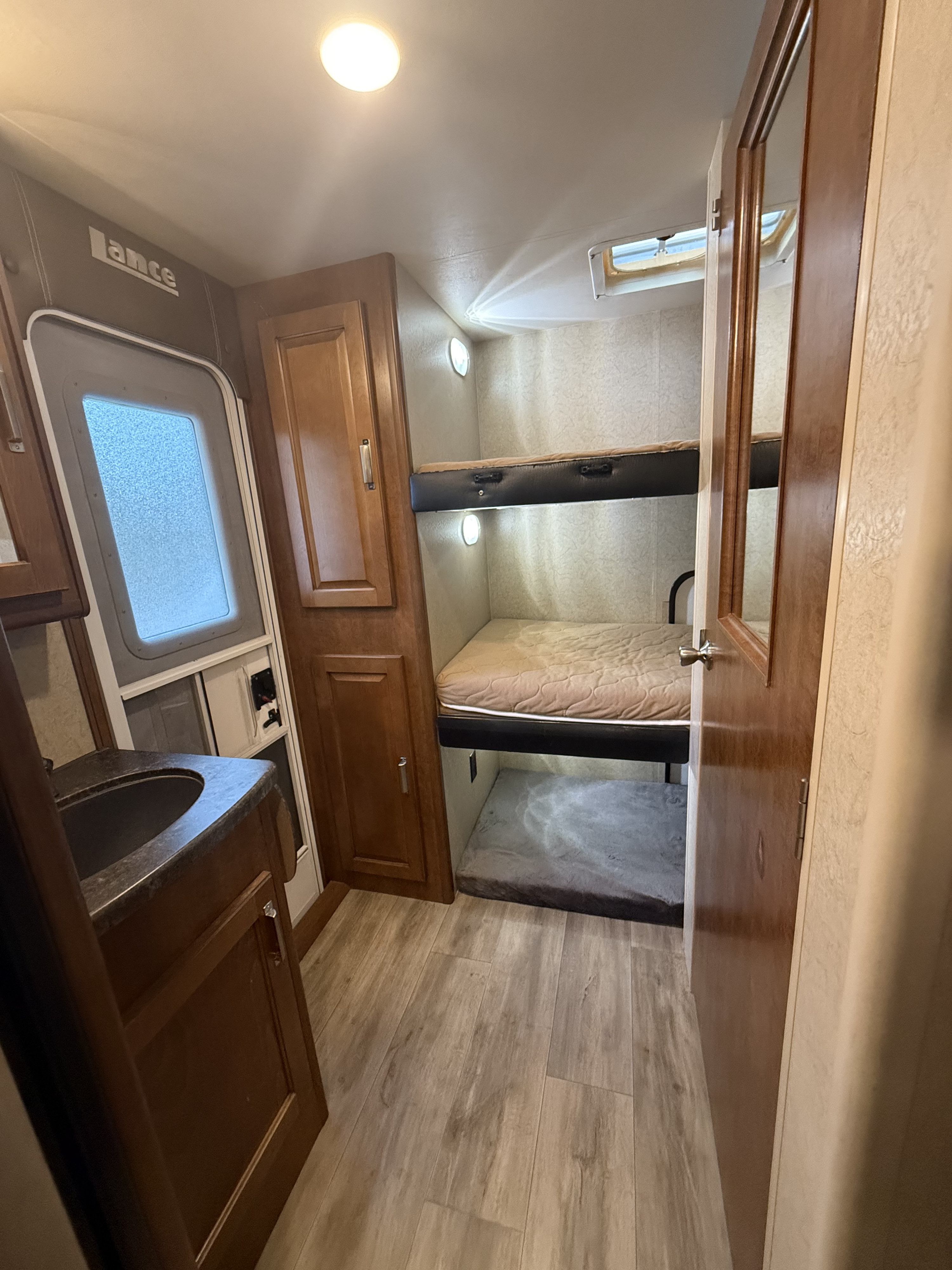 RV rental interior showing two bunk beds with mattresses, a sink counter, and wood-look flooring. Cozy compact space.. Lance Manufacturing Lance Manufacturing Trailer 2017