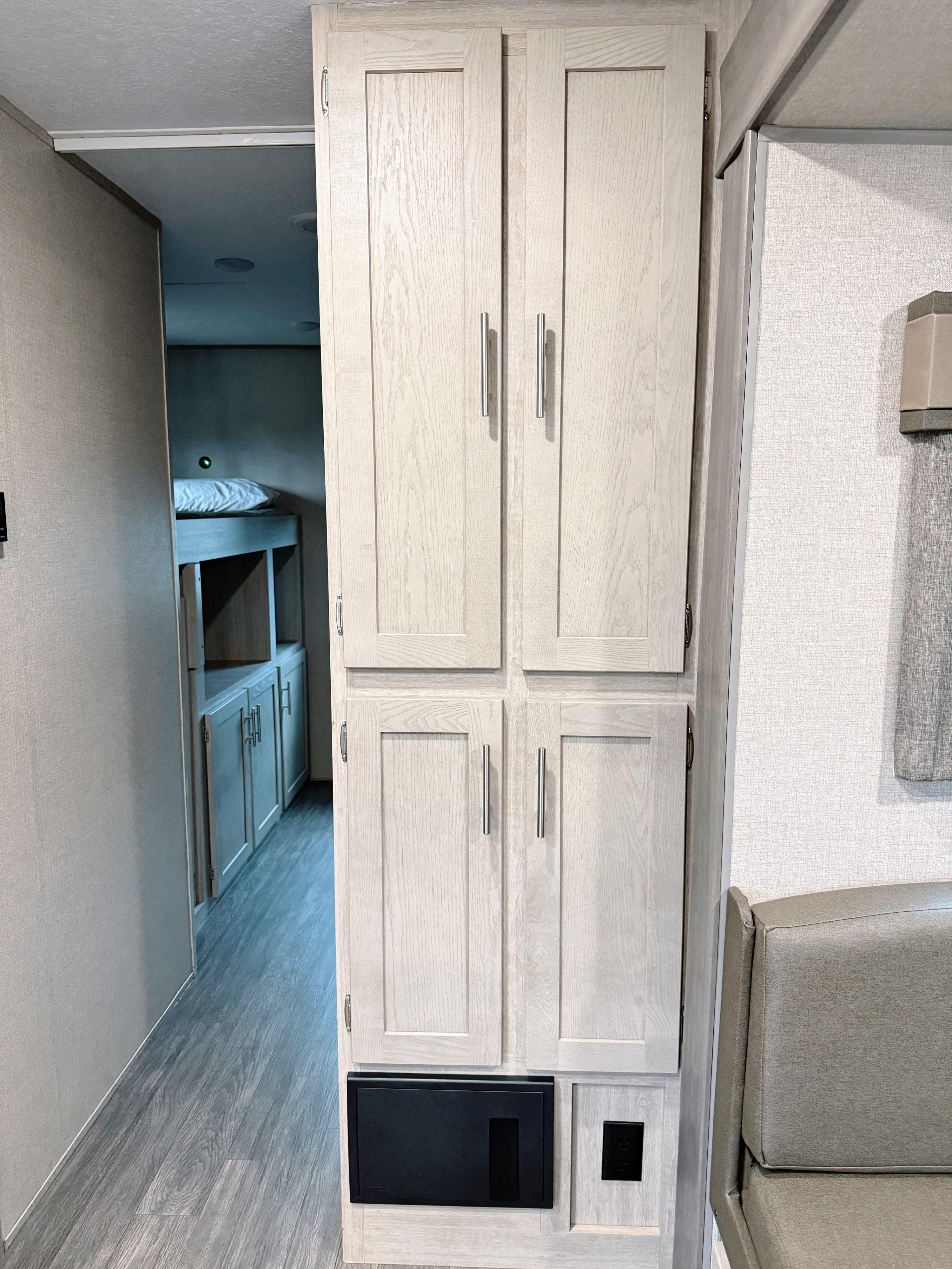 Inside an RV rental: light wood cabinets and a gray seating area in the foreground, with bunk beds visible down the hallway.. Forest River Aurora Sky Series 2023