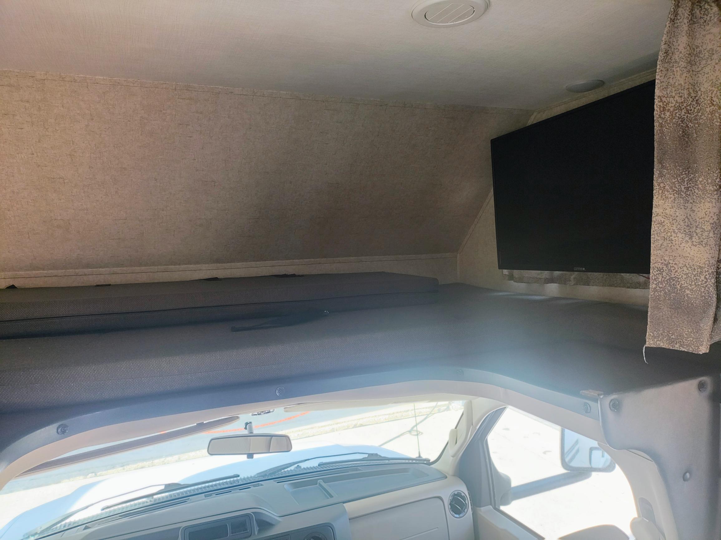 Inside an RV rental, showing the cozy overhead bunk and TV above the driver's area, ready for adventure.. Forest River Sunseeker LE 2020