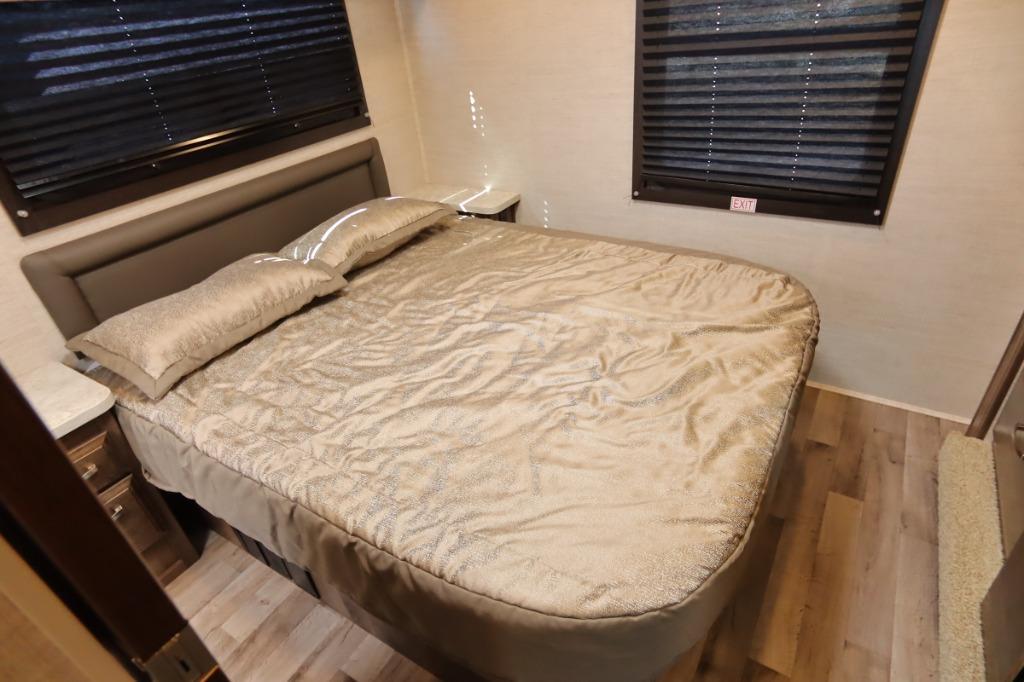 Cozy RV rental bedroom features a comfortable bed, padded headboard, nightstands, and window blinds for your next adventure.. Jayco Redhawk 2021