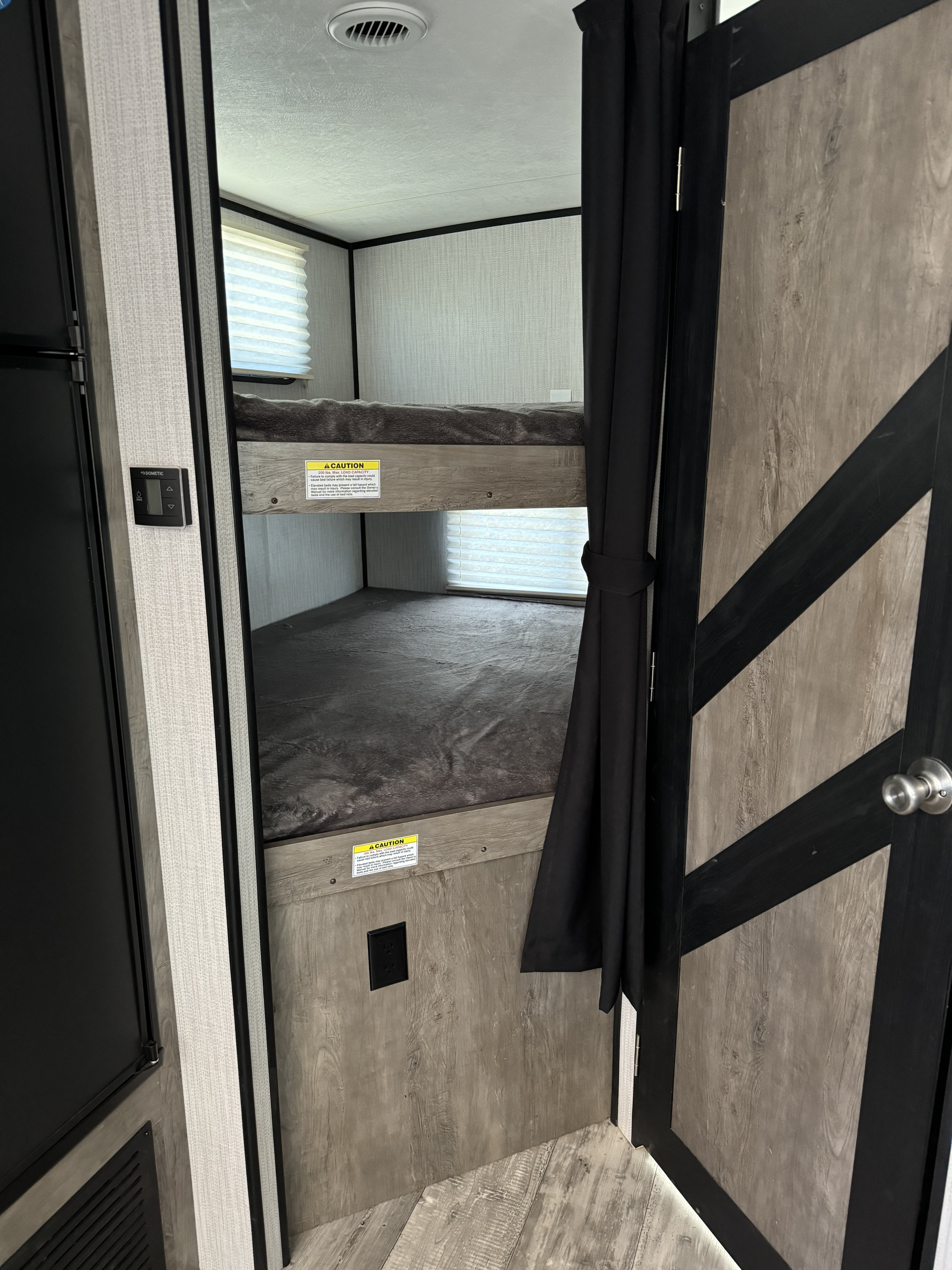 Compact RV rental interior showcasing cozy bunk beds with grey bedding, a Dometic thermostat, and modern wood-look panels.. Heartland RVs North Trail 2021