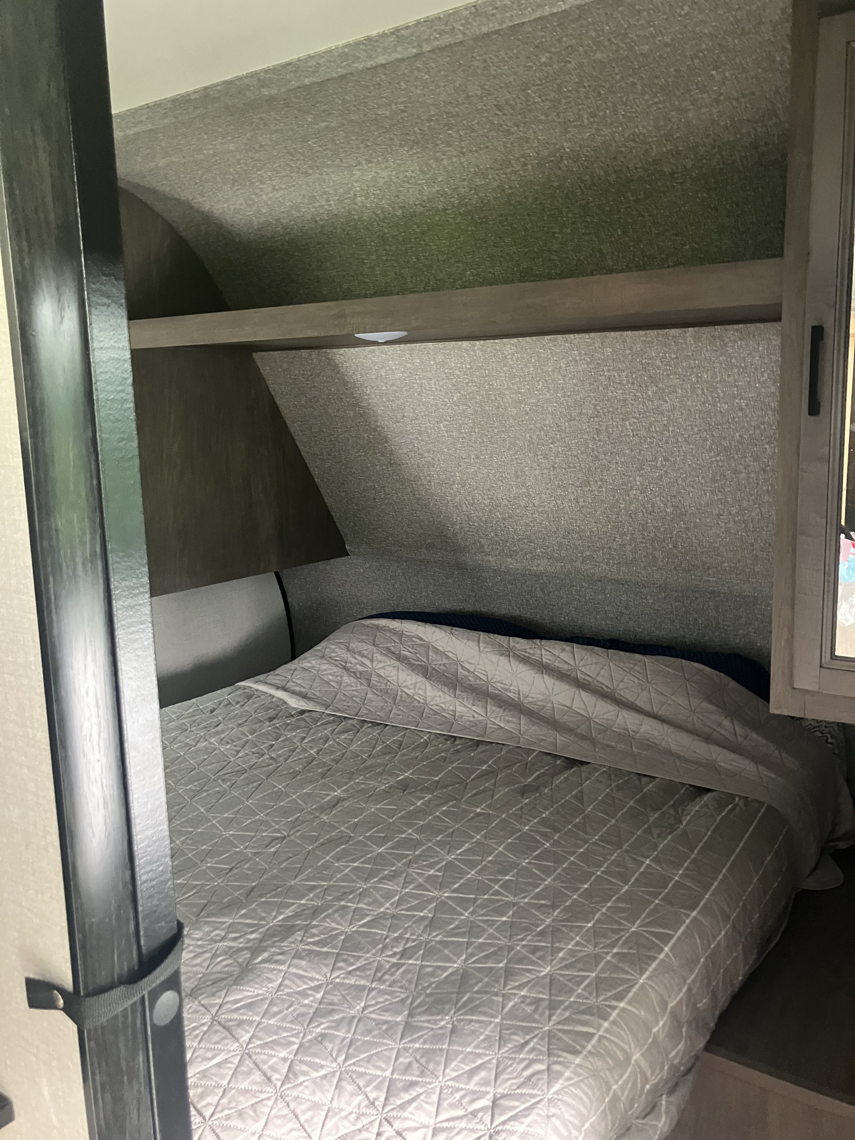 View of an RV rental bedroom with a grey quilted bed, overhead shelf with light, and textured walls.. Starcraft Autumn Ridge 2022