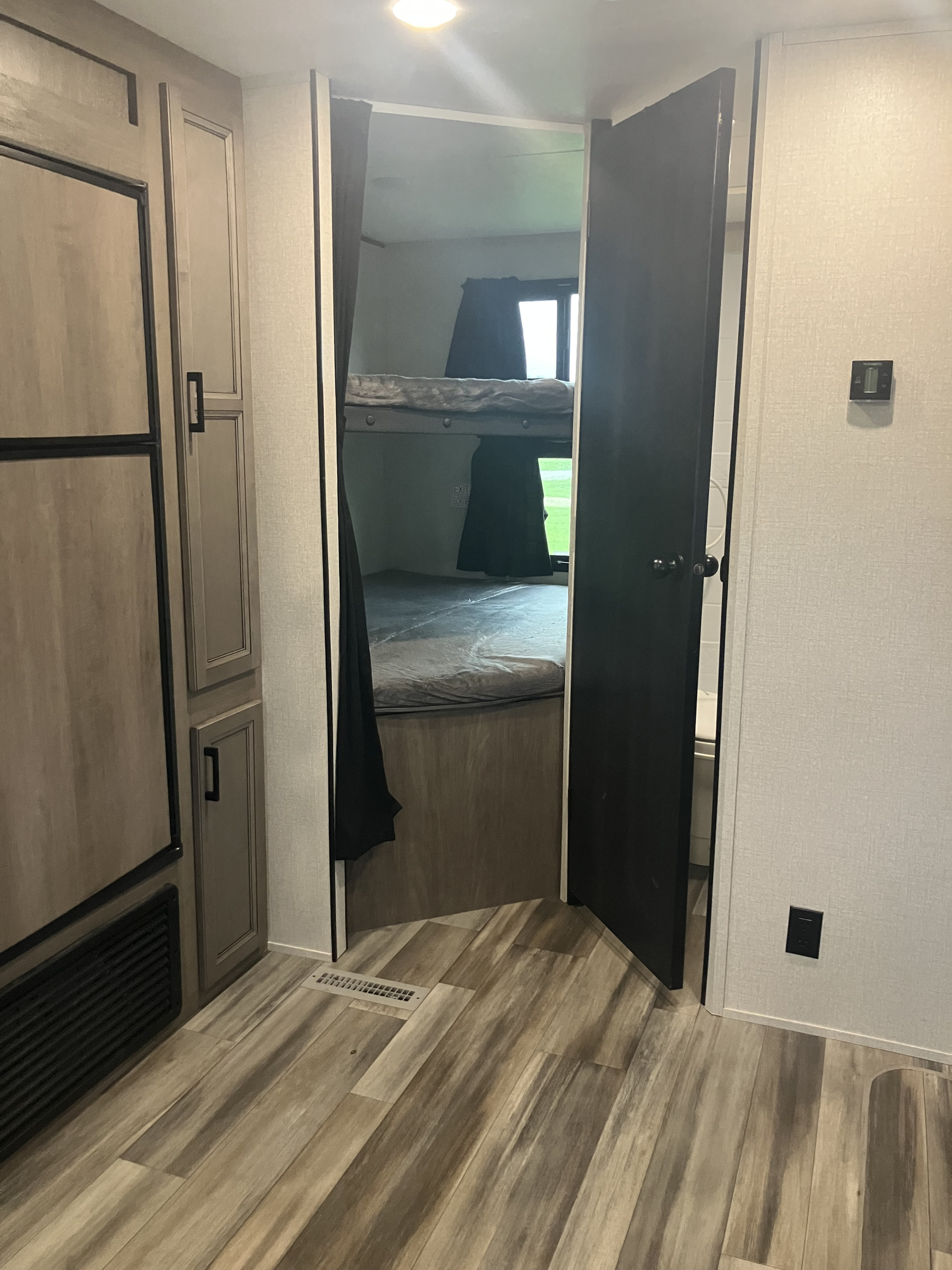 RV rental interior featuring a view of the cozy bunk beds through an open doorway, with wood-look flooring and built-in cabinetry.. Starcraft Autumn Ridge 2022