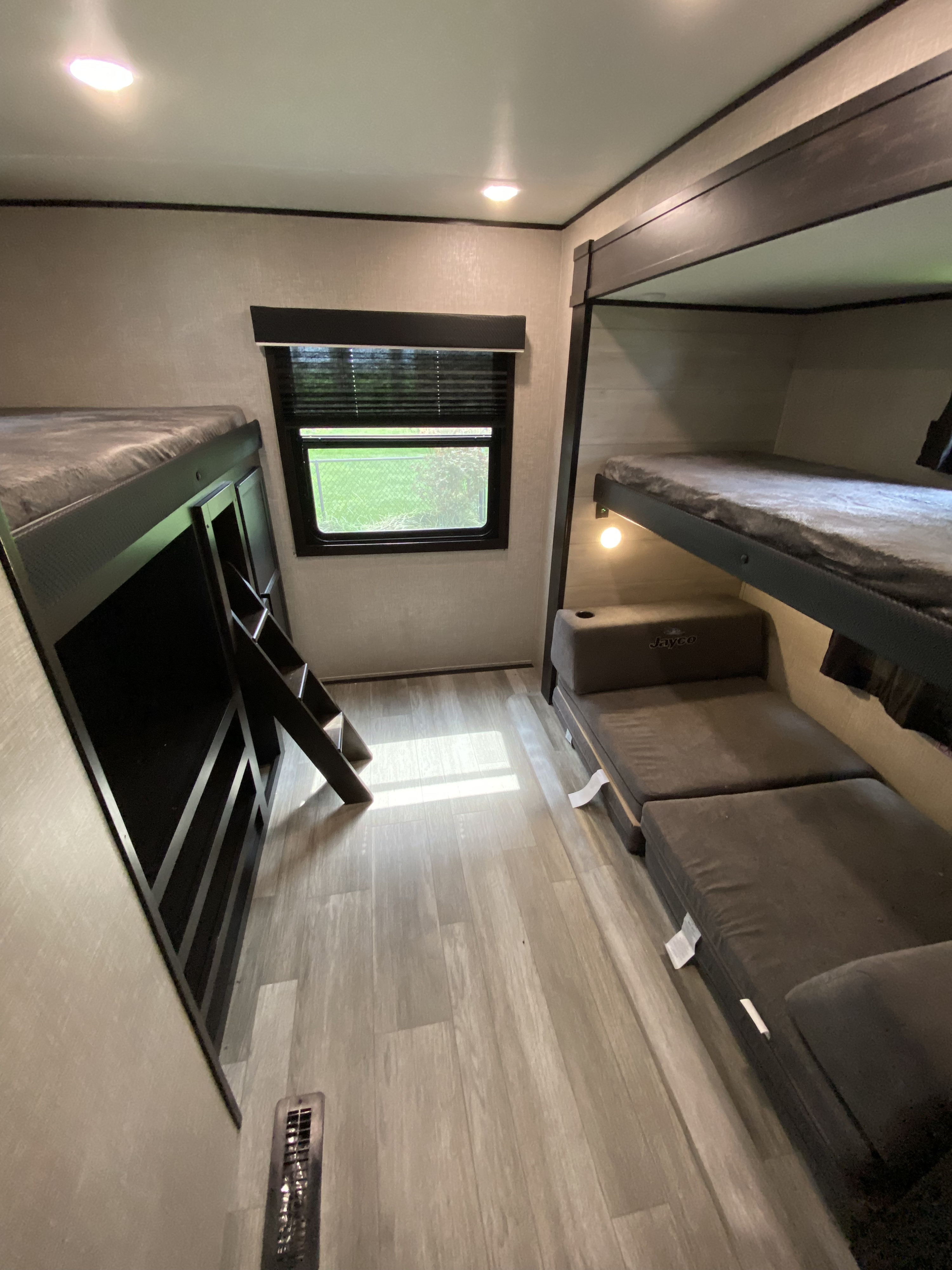 This RV rental bunkhouse features a double bunk bed setup on the left, an upper bunk with convertible seating on the right, a window, and light wood flooring.. Jayco Jay Flight SLX 2022
