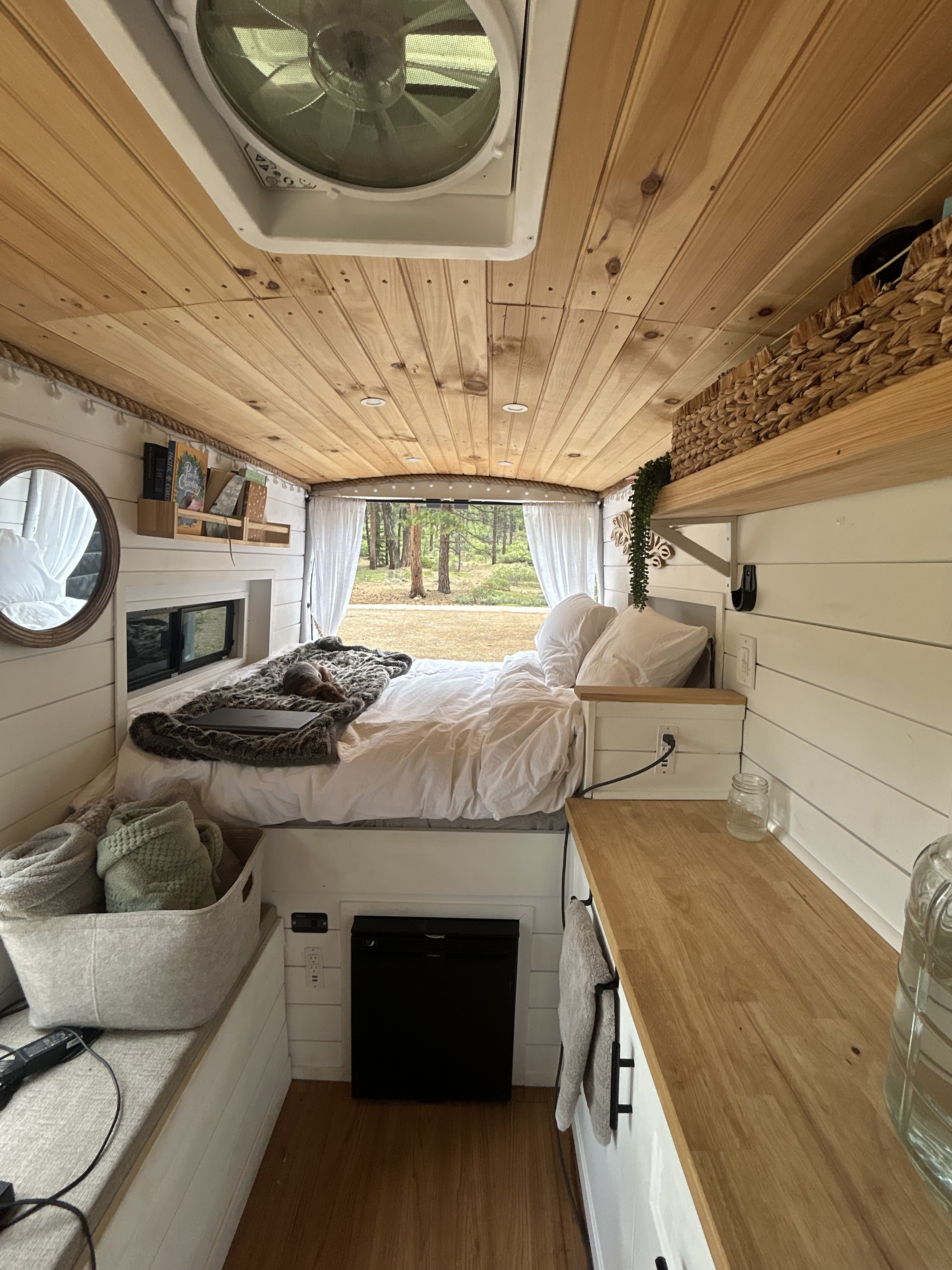 Cozy RV rental interior: wooden ceiling, comfy bed, compact kitchen, and serene forest views from the back.. Ford Transit 2020