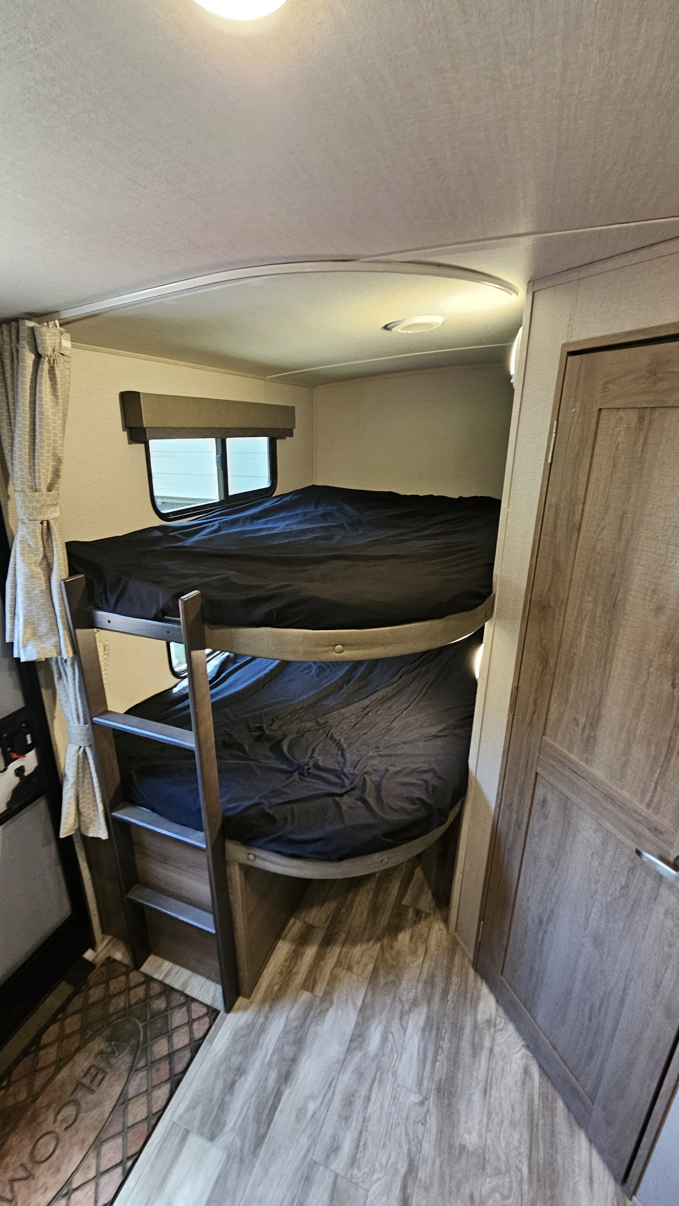 Inside an RV rental: two cozy bunk beds with dark sheets, a ladder, window, and wood-style floor.. Grand Design Imagine 2021