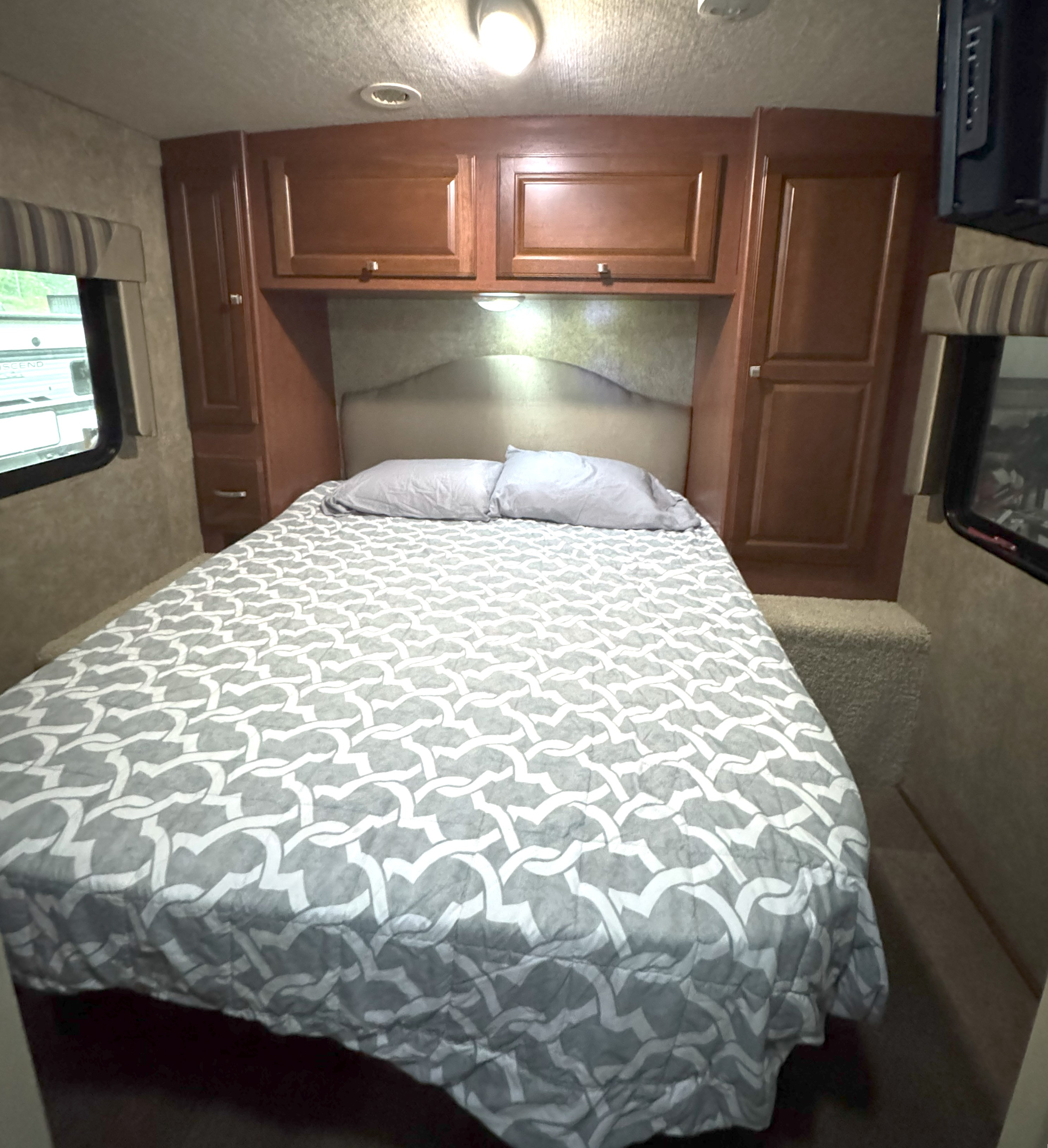 RV rental bedroom featuring a cozy bed with patterned comforter, wooden cabinets, and a window. Perfect for your next adventure!. Itasca Sunstar 2014