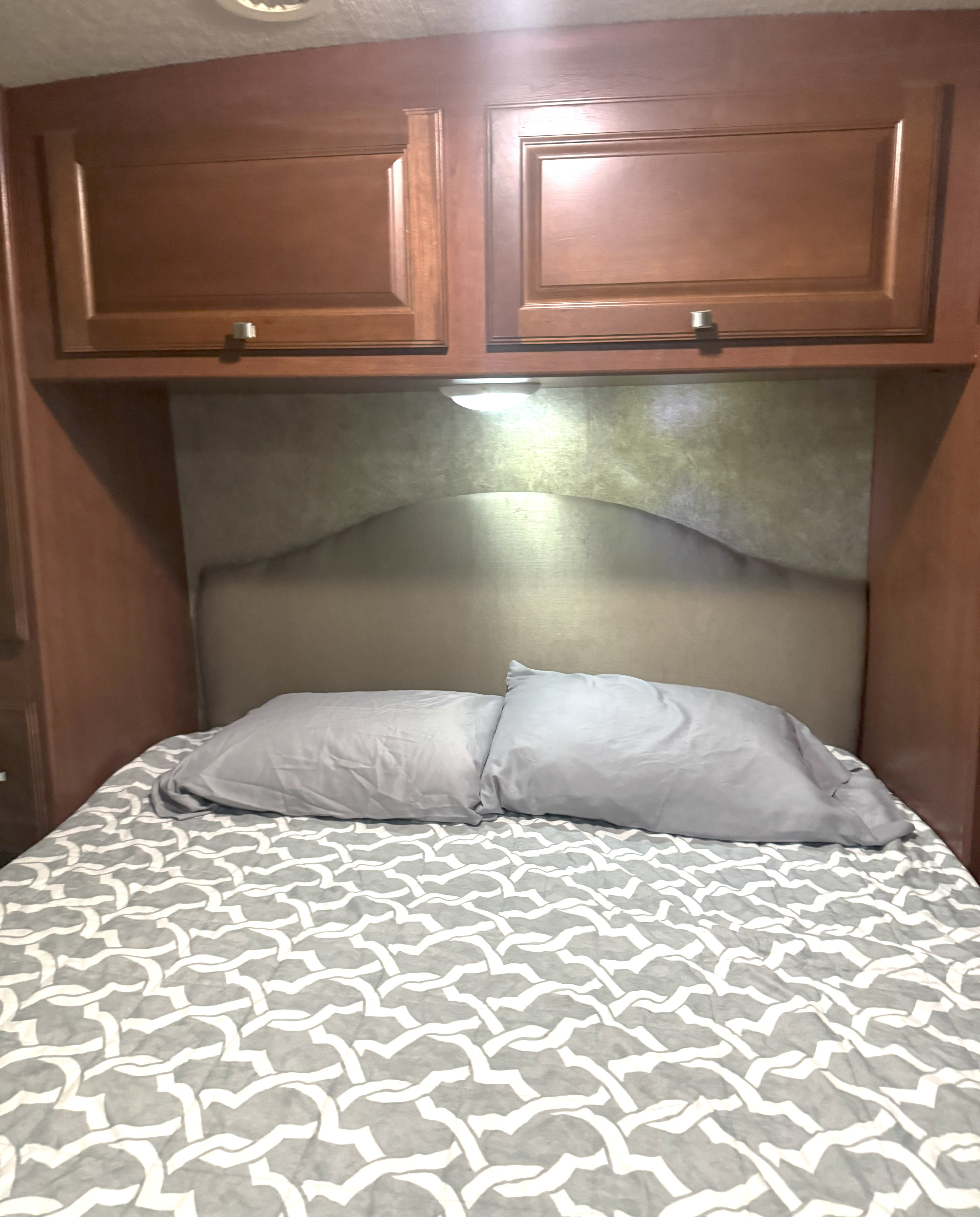 Cozy rv rental bedroom featuring a bed with patterned bedding, headboard, and storage cabinets with lighting.. Itasca Sunstar 2014