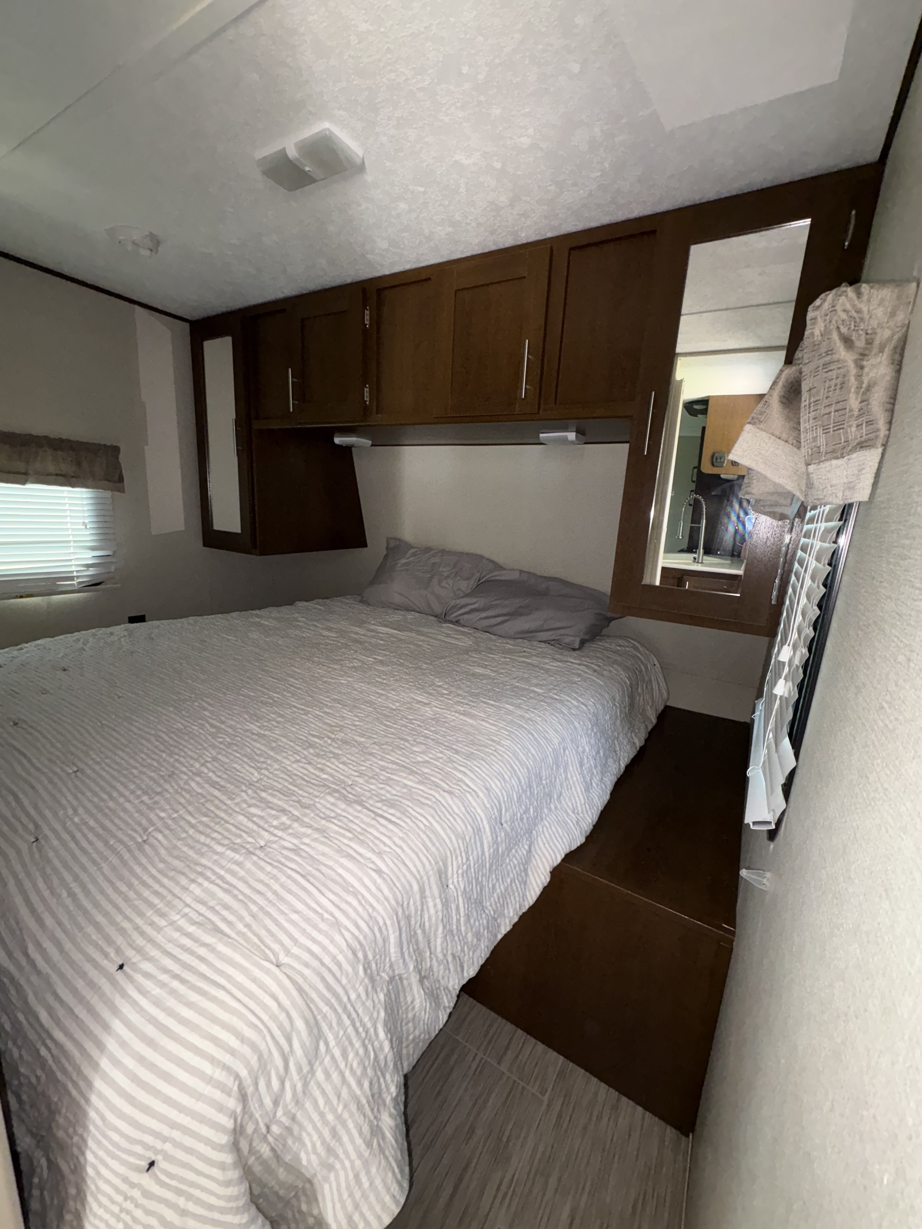 Compact RV rental bedroom with striped bed, overhead storage, and a mirrored cabinet reflecting the kitchen space.. Avenger ATI 2018
