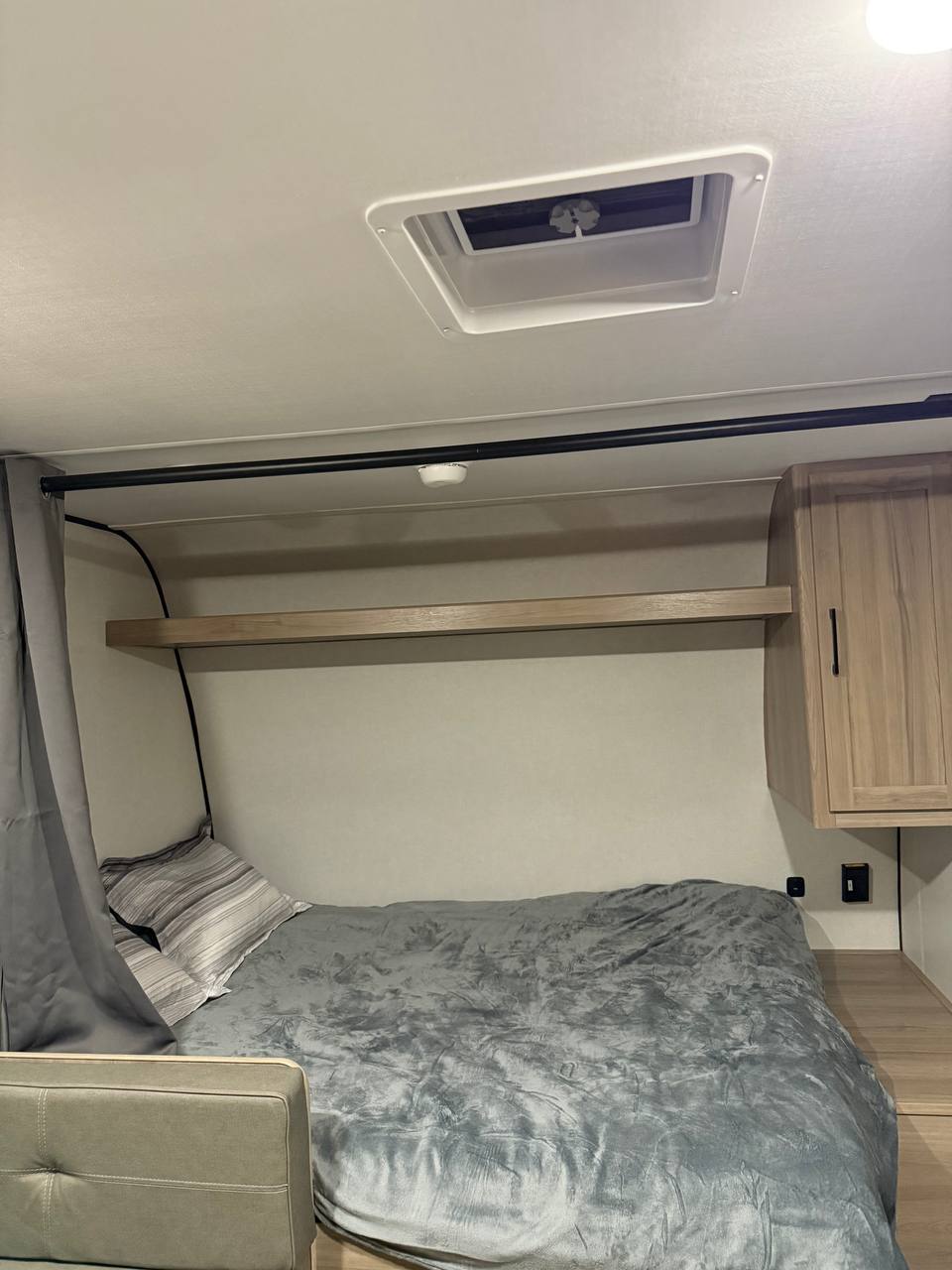 Cozy RV rental bedroom with a plush gray bed, wood shelf, and cabinet, showing a compact, functional sleeping space.. Coleman Light 17BX 2025