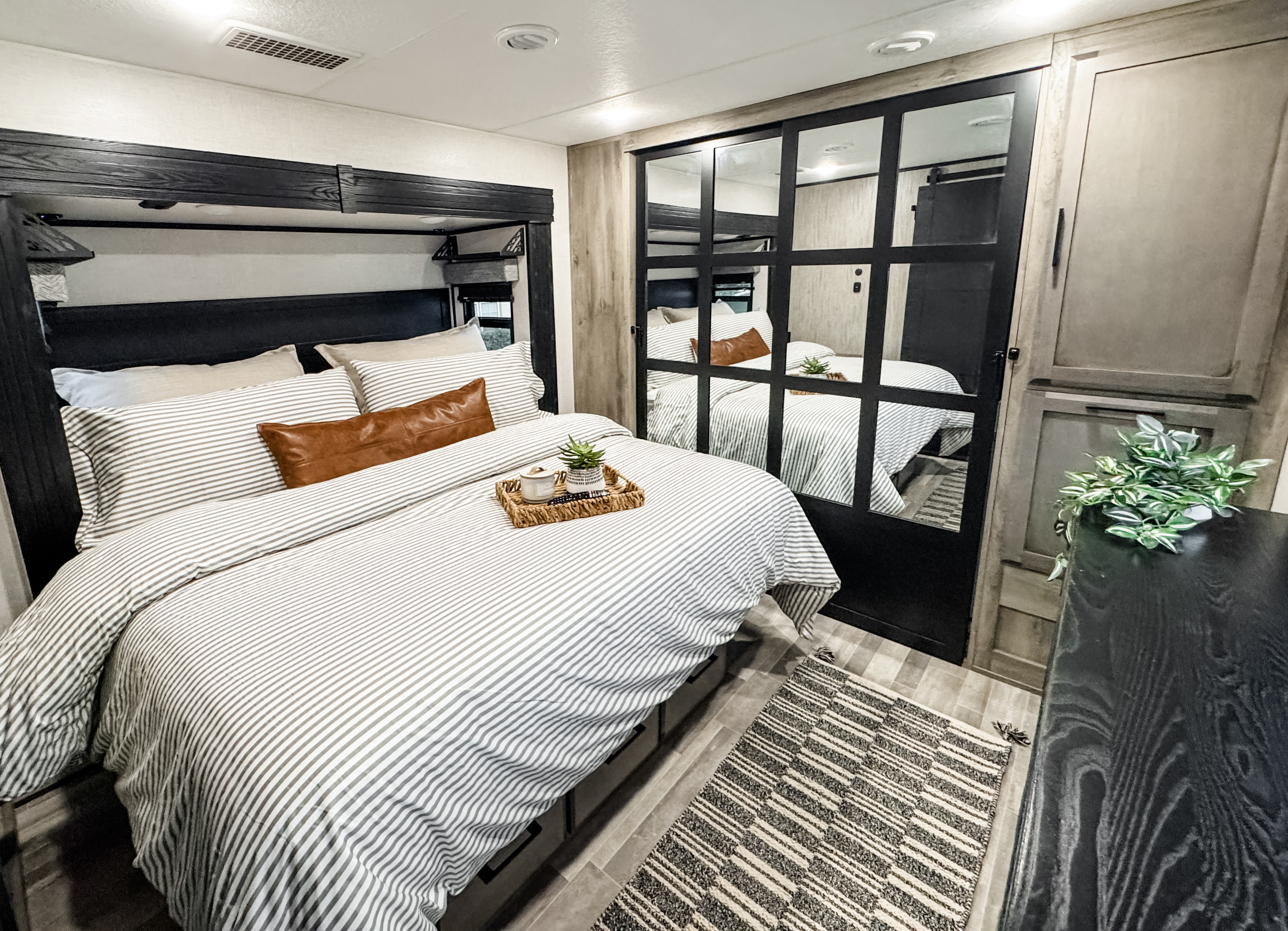Relax in this inviting RV rental bedroom, featuring striped bedding, warm accents, and a mirrored closet for functional storage.. Durango Gold 2023