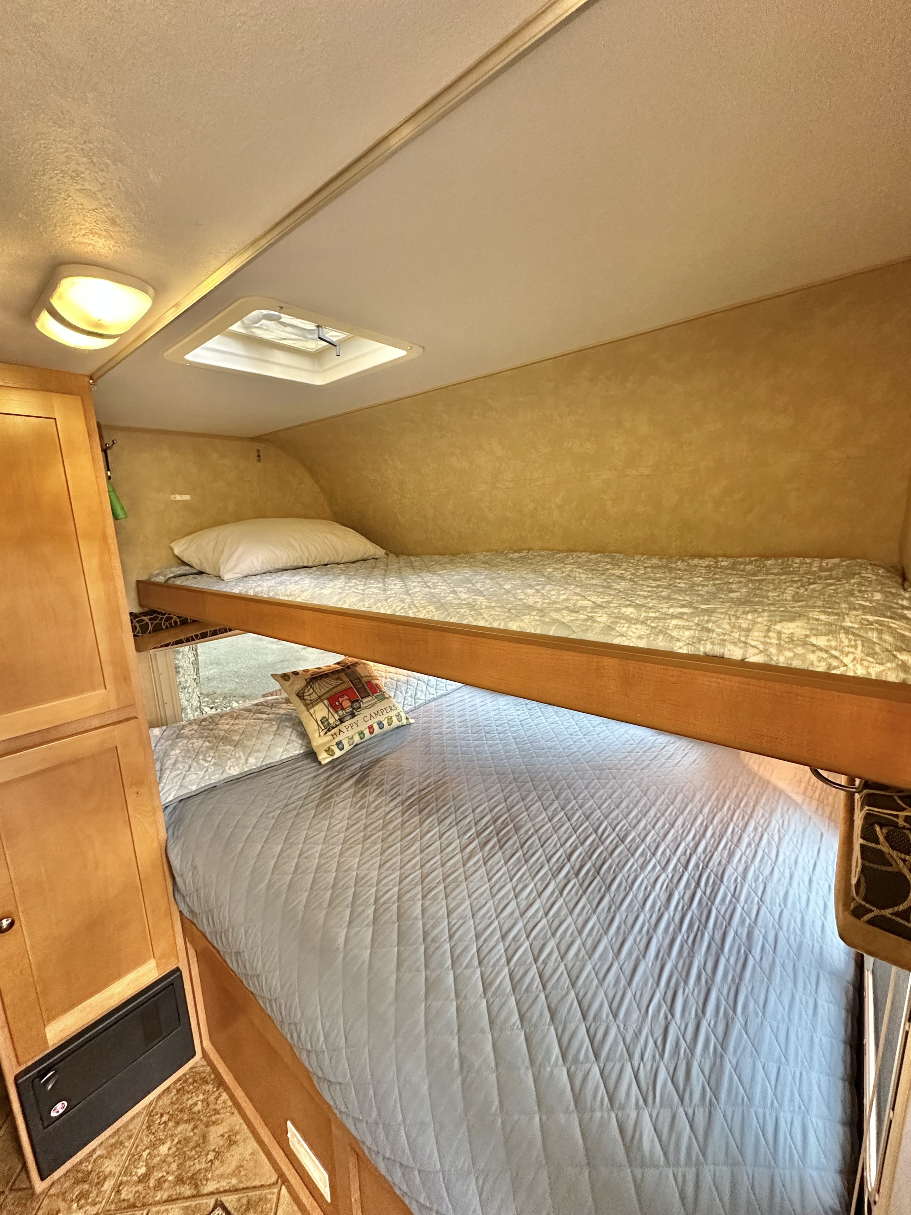Cozy RV rental interior with two bunk beds. Features light blue and white quilted bedding, a window, and wood cabinetry.. Cruiser RV Fun Finder X 2011