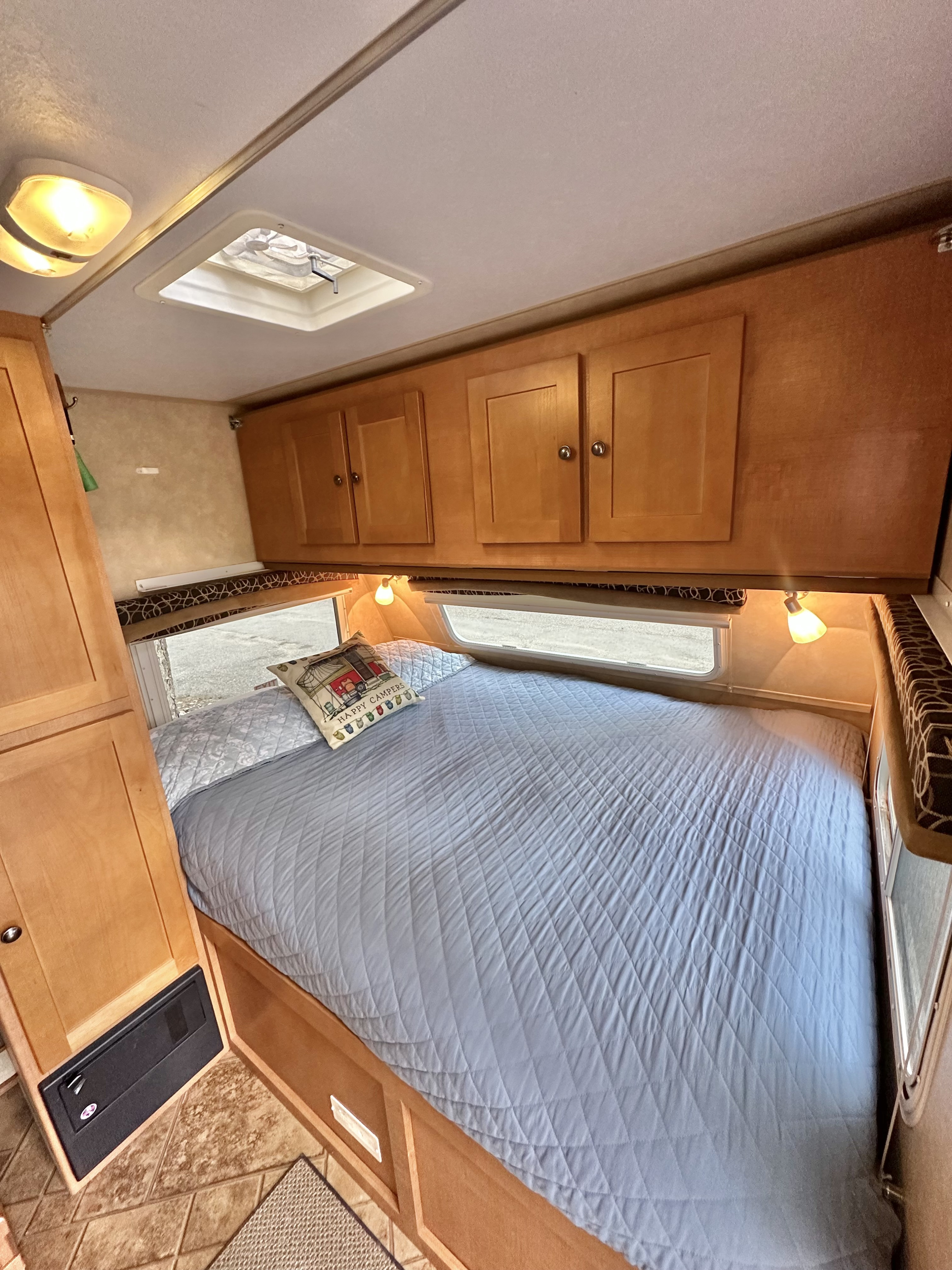 Comfortable RV rental bedroom featuring a quilted bed, overhead wooden cabinets, and a ceiling skylight.. Cruiser RV Fun Finder X 2011