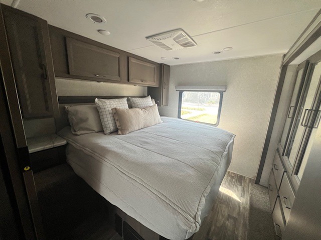 Cozy RV rental bedroom featuring a comfortable bed, overhead storage, and natural light from a window.. Thor Hurricane 2023