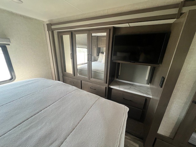Inside a cozy RV rental bedroom, showing the bed, mirrored wardrobe, and TV area.. Thor Hurricane 2023