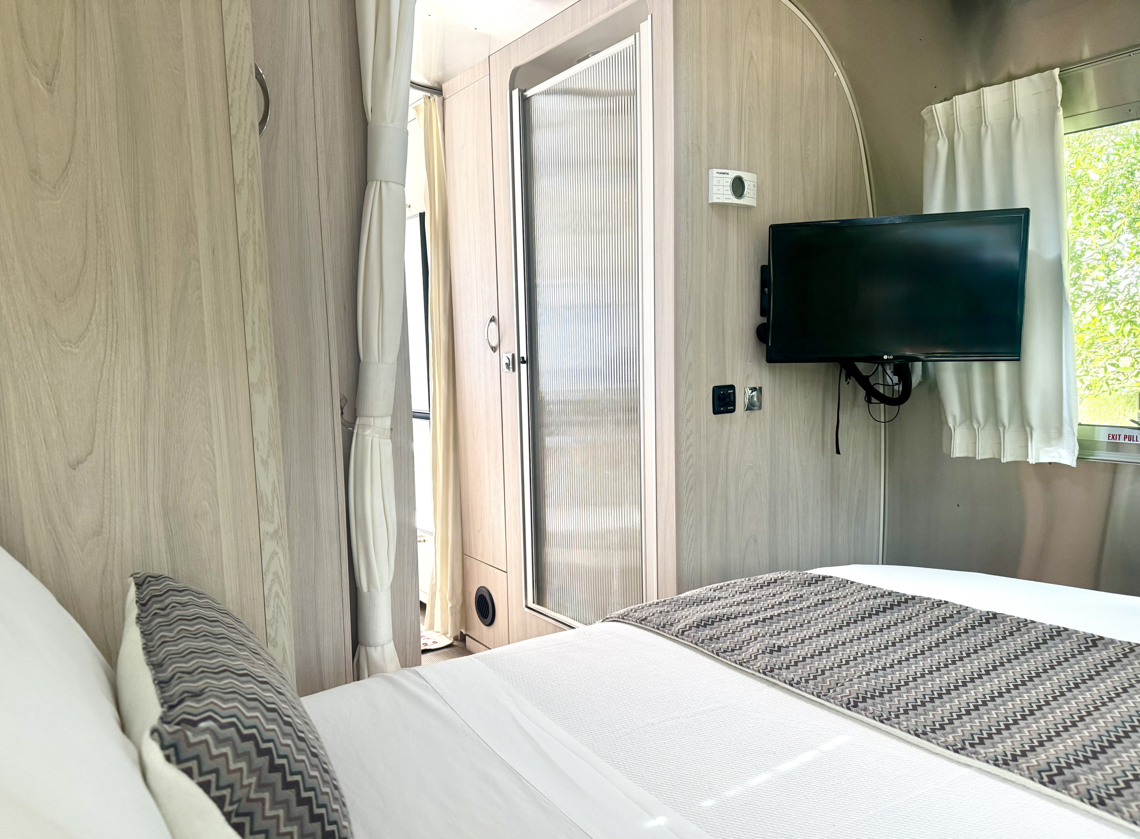 Modern Airstream RV rental interior: bedroom with TV, compact shower, and light wood finishes. Comfortable travel.. Airstream Globetrotter 2021