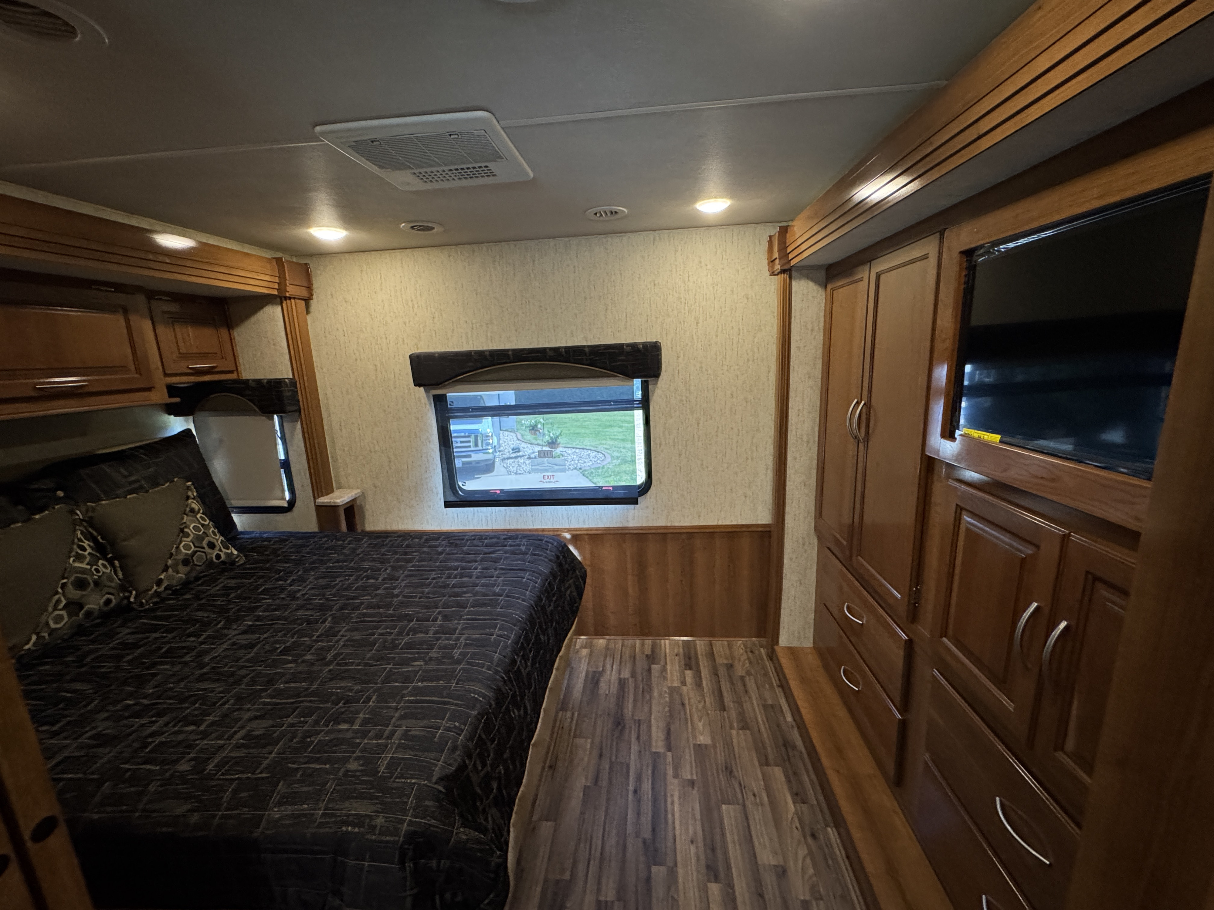 Comfortable RV rental bedroom featuring a large bed, built-in wooden cabinets, TV, and windows with outdoor views. Ideal for travel.. Coachmen Forest River 2018