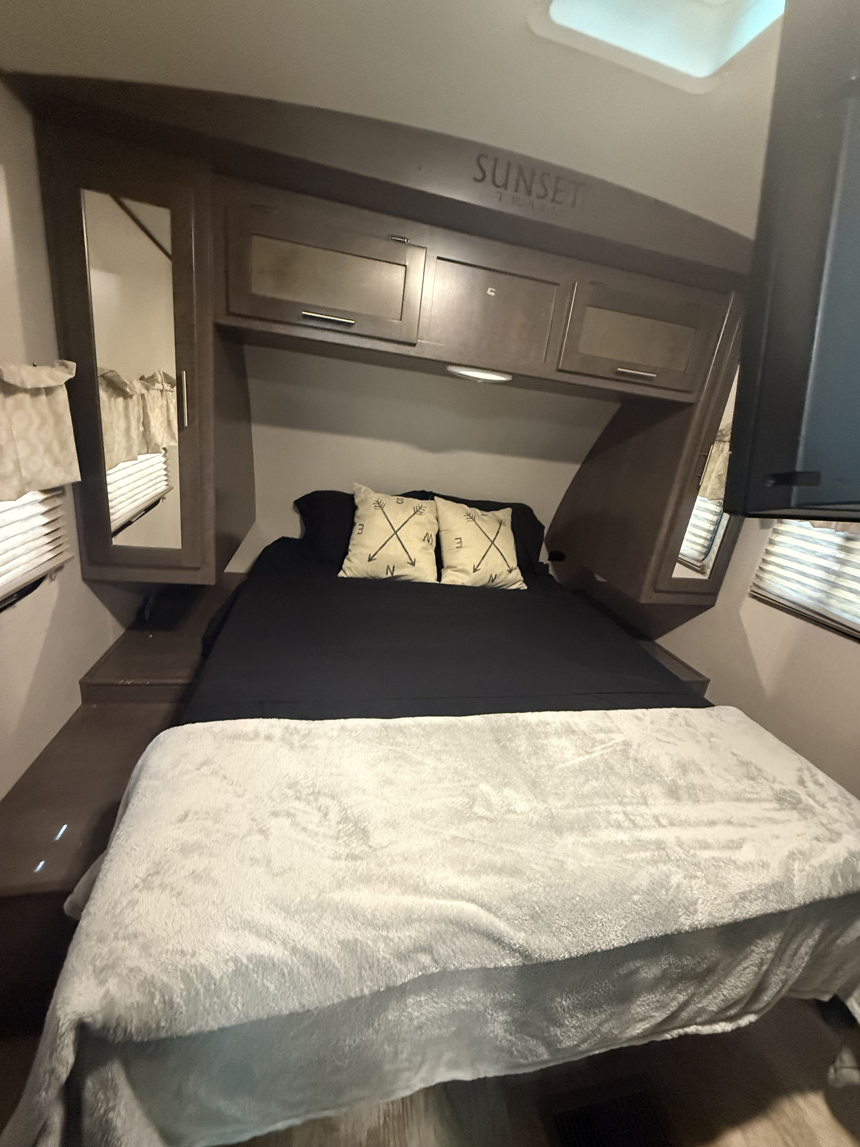 Inside a cozy RV bedroom with a bed, decorative pillows, overhead storage, and mirrored cabinets. Ideal for an rv rental.. Crossroads RV Sunset Trail Super Lite 2018