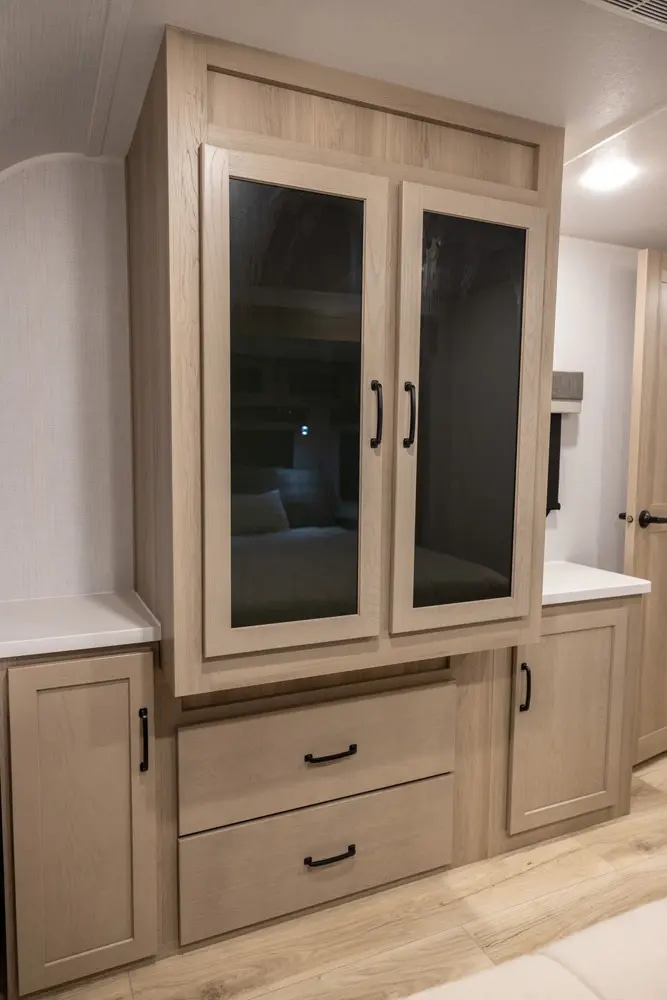 Modern light wood cabinets and drawers in an RV rental, with glass doors reflecting a bedroom area inside.. Forest River Rockwood Ultra Lite 2024