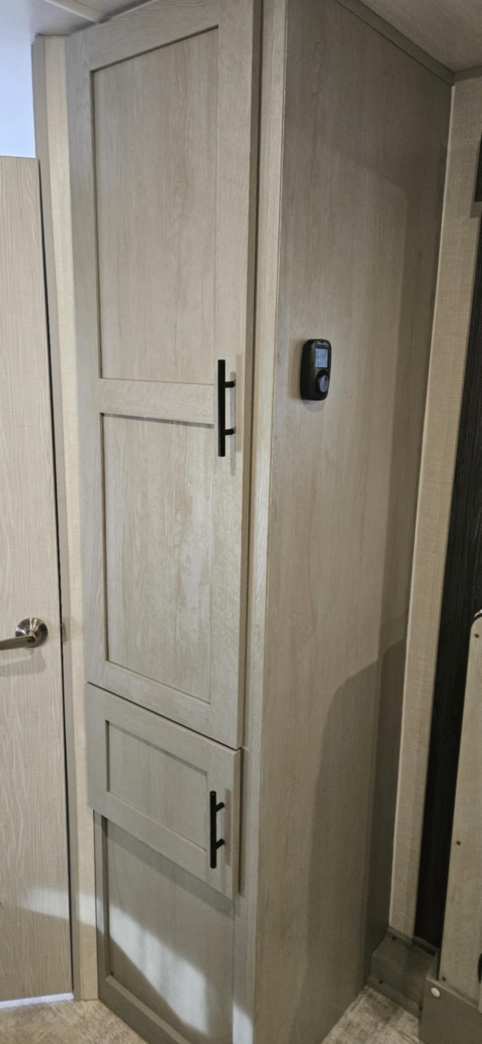 Tall light wood cabinet and digital thermostat in an RV rental, providing essential controls and storage in a compact space.. Forest River Ibex Essentials+ Only 2024