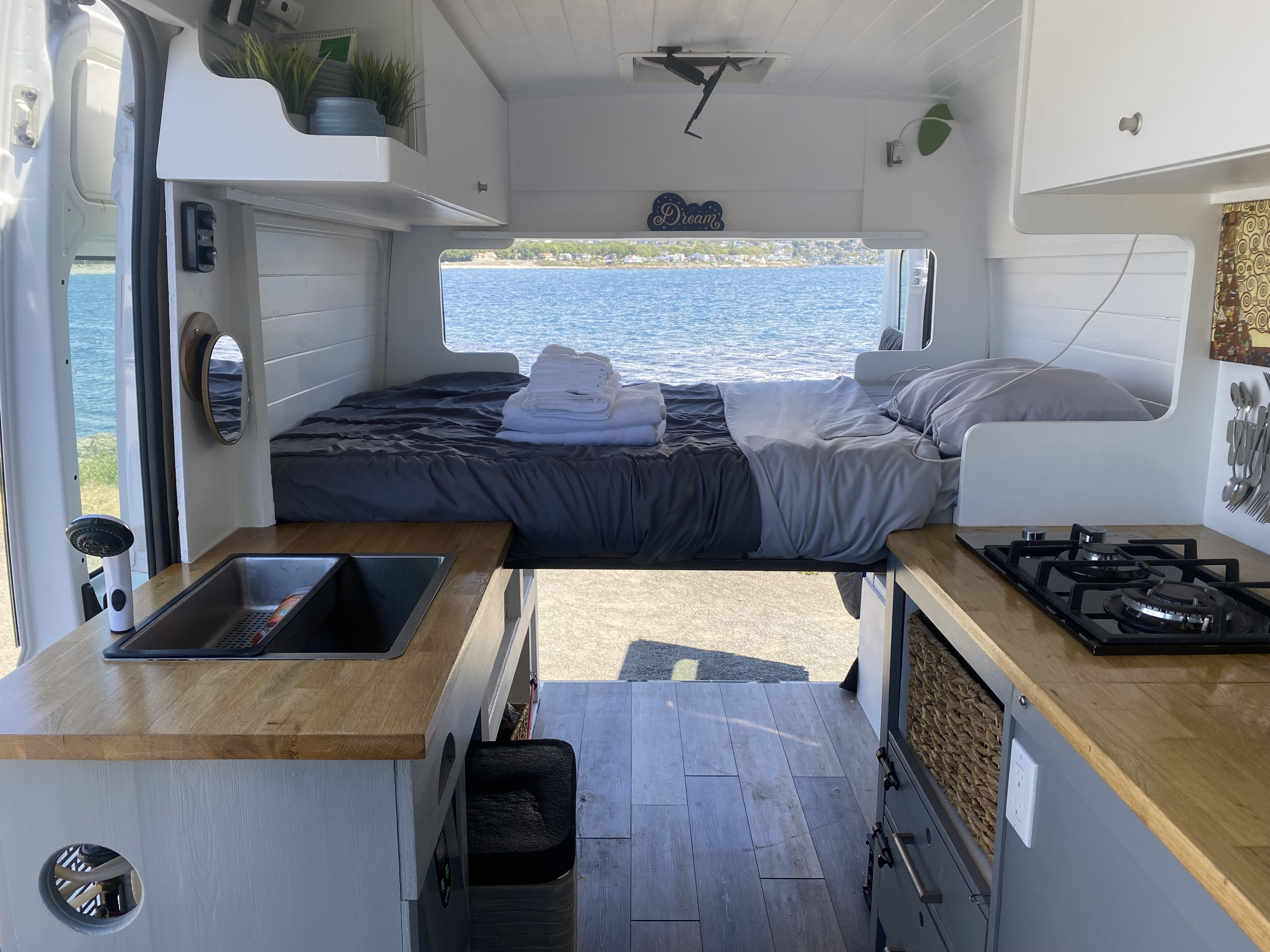 Spacious and cozy RV rental interior with ocean view bed, full kitchen, and stylish design, perfect for van life adventures.. Ram Promaster 2014