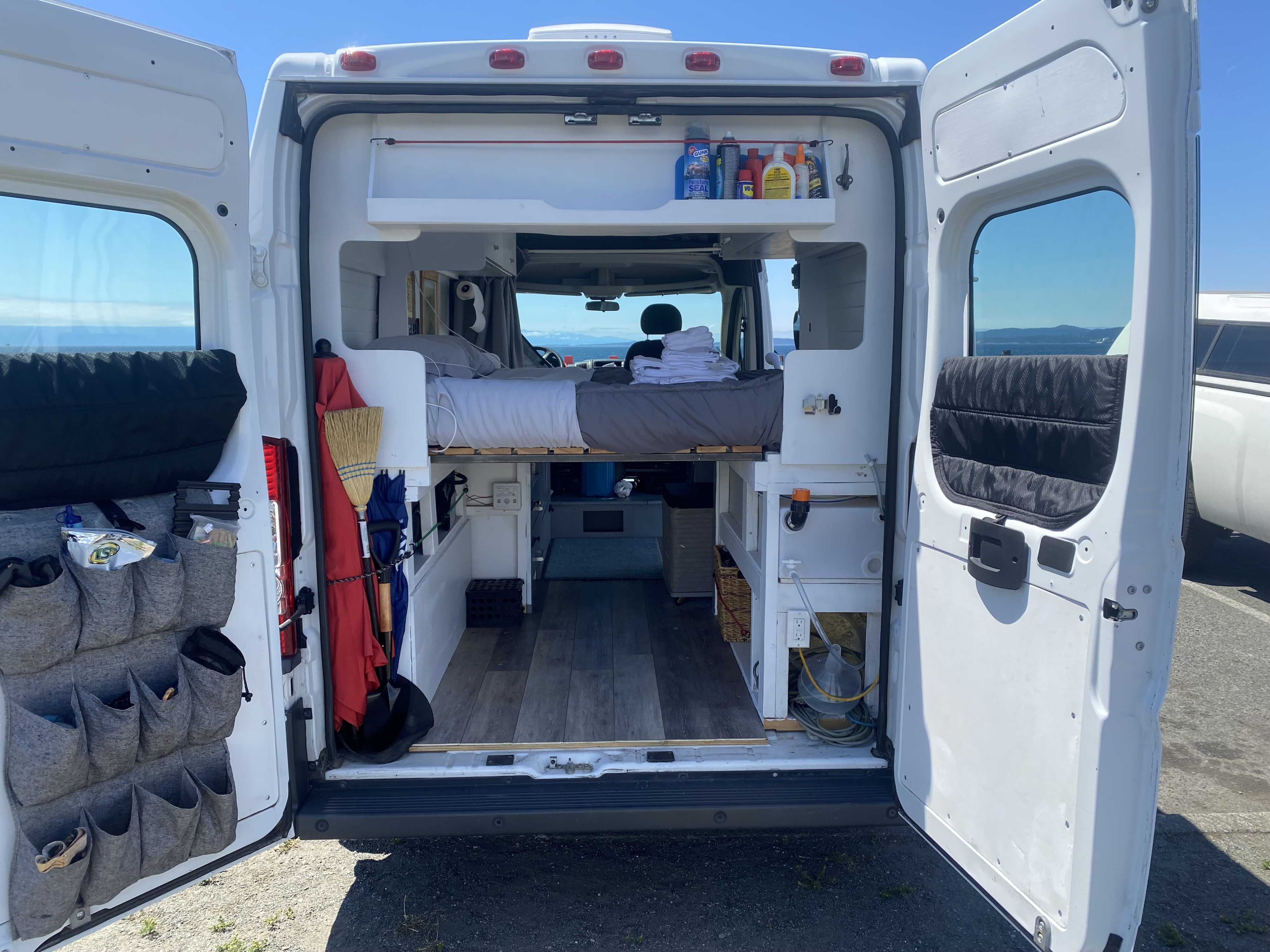 RV rental: Organized camper van interior with bed, storage, and ocean view from open rear doors.. Ram Promaster 2014