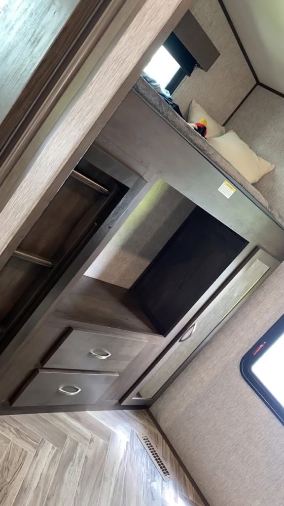 RV rental interior features: bunk bed, built-in closet, open storage, and two lower drawers. Light wood floor, neutral walls.. Dutchmen Astoria 2021