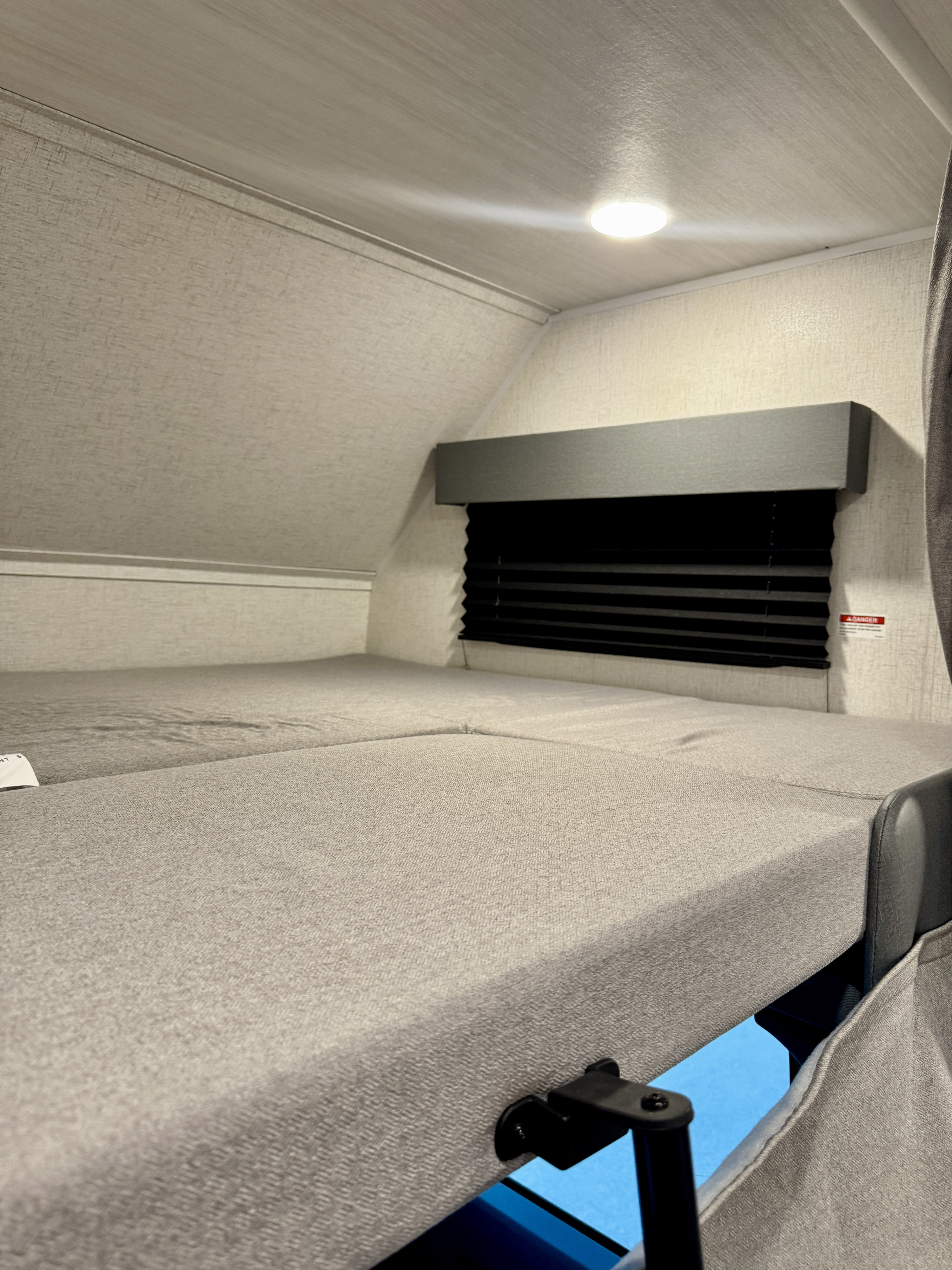 Cozy RV rental sleeping area with light-colored cushions and a window with black blinds, illuminated by an overhead light.. Entrada Entrada Motorhome 2022