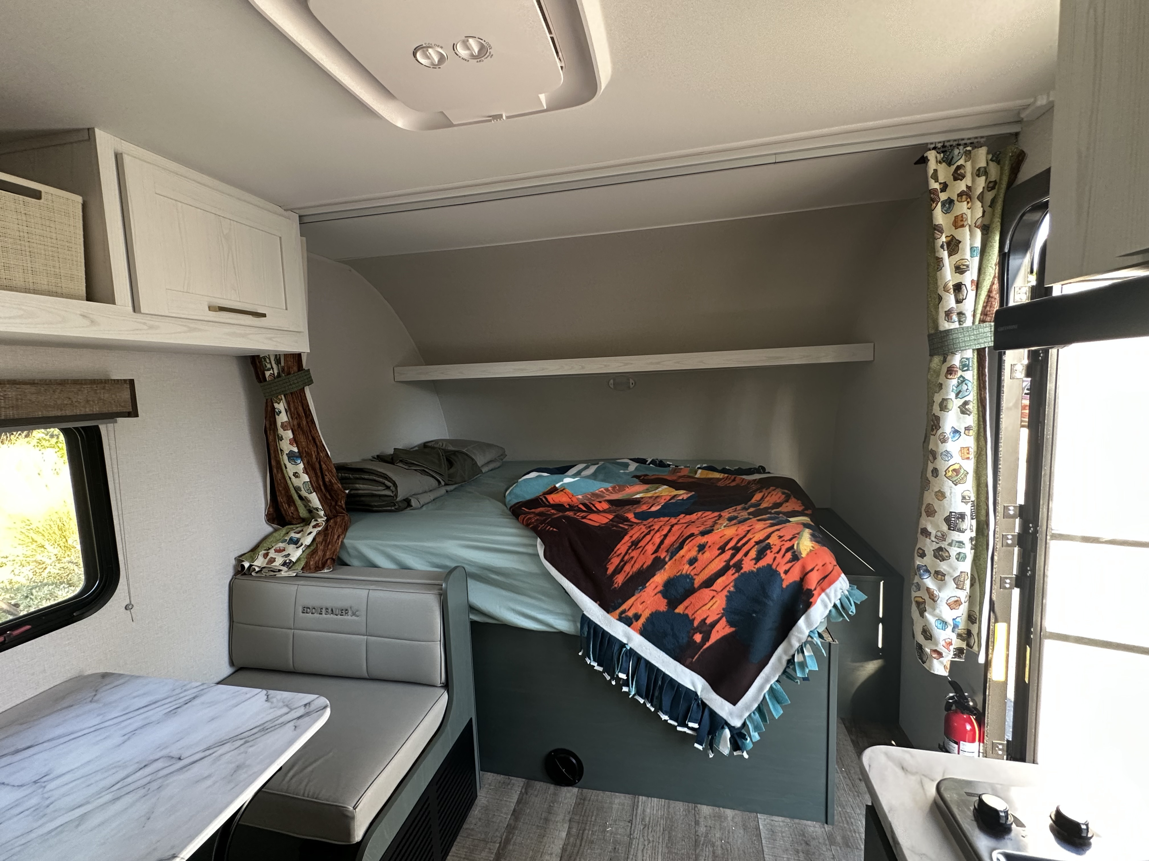 Cozy RV rental interior showing a bed, dinette with table, and compact kitchen area. Ideal for travel.. Heartland Eddie Bauer 2025