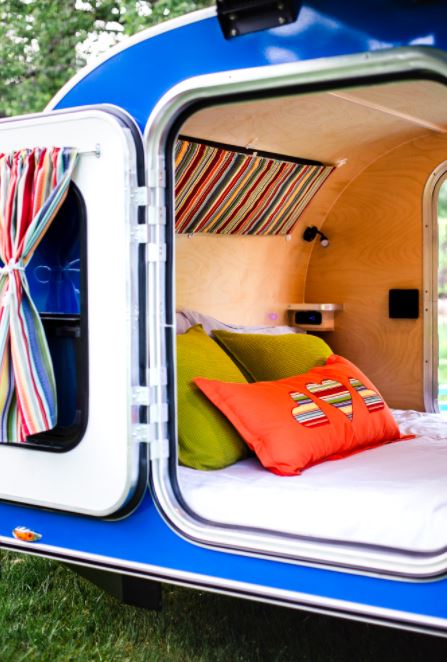 Cozy teardrop RV rental interior with a comfy bed, green & orange pillows, and colorful striped accents.. Aero Steel 2021